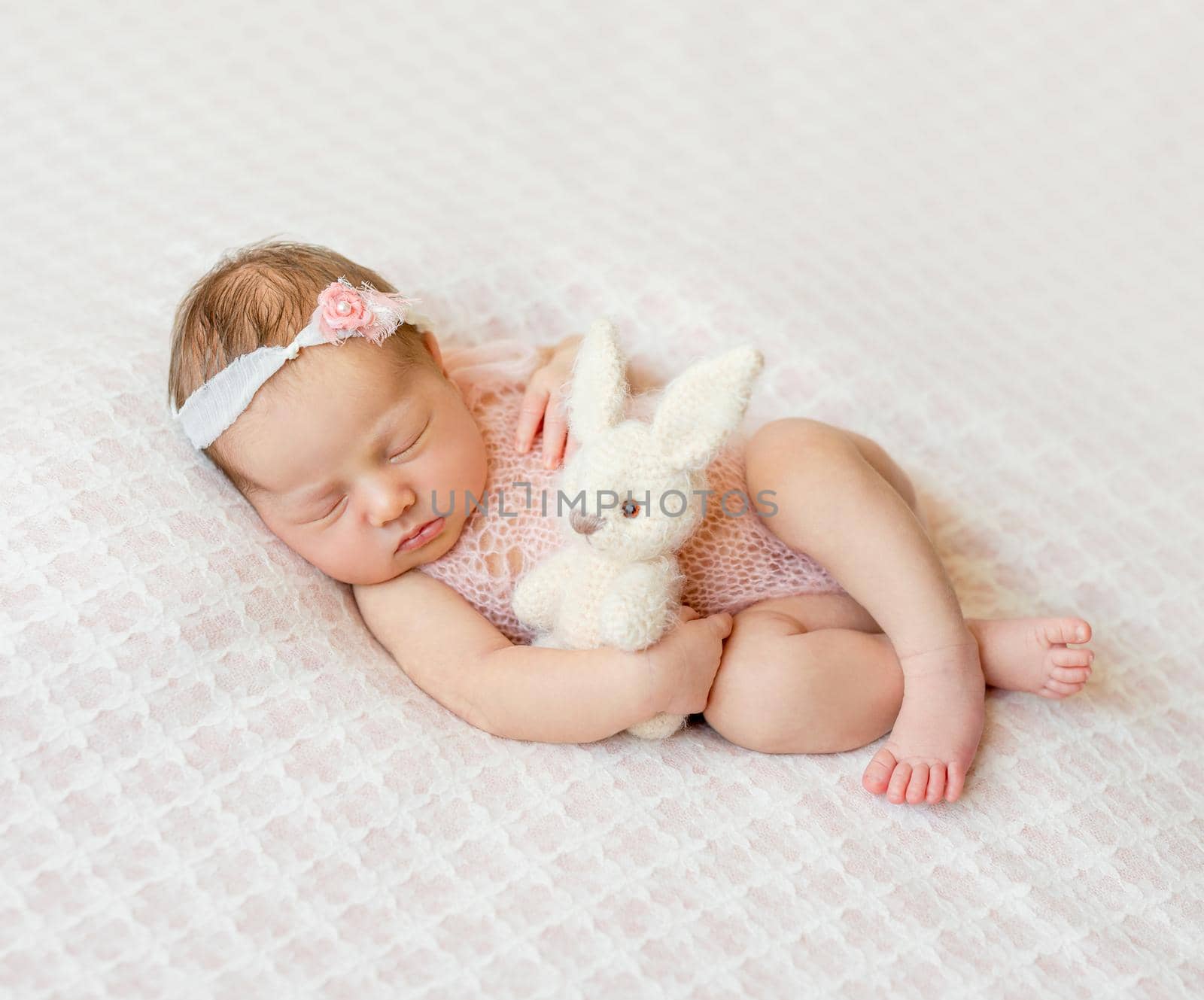 lovely sleeping newborn girl with headband and holding toy on pink blanket
