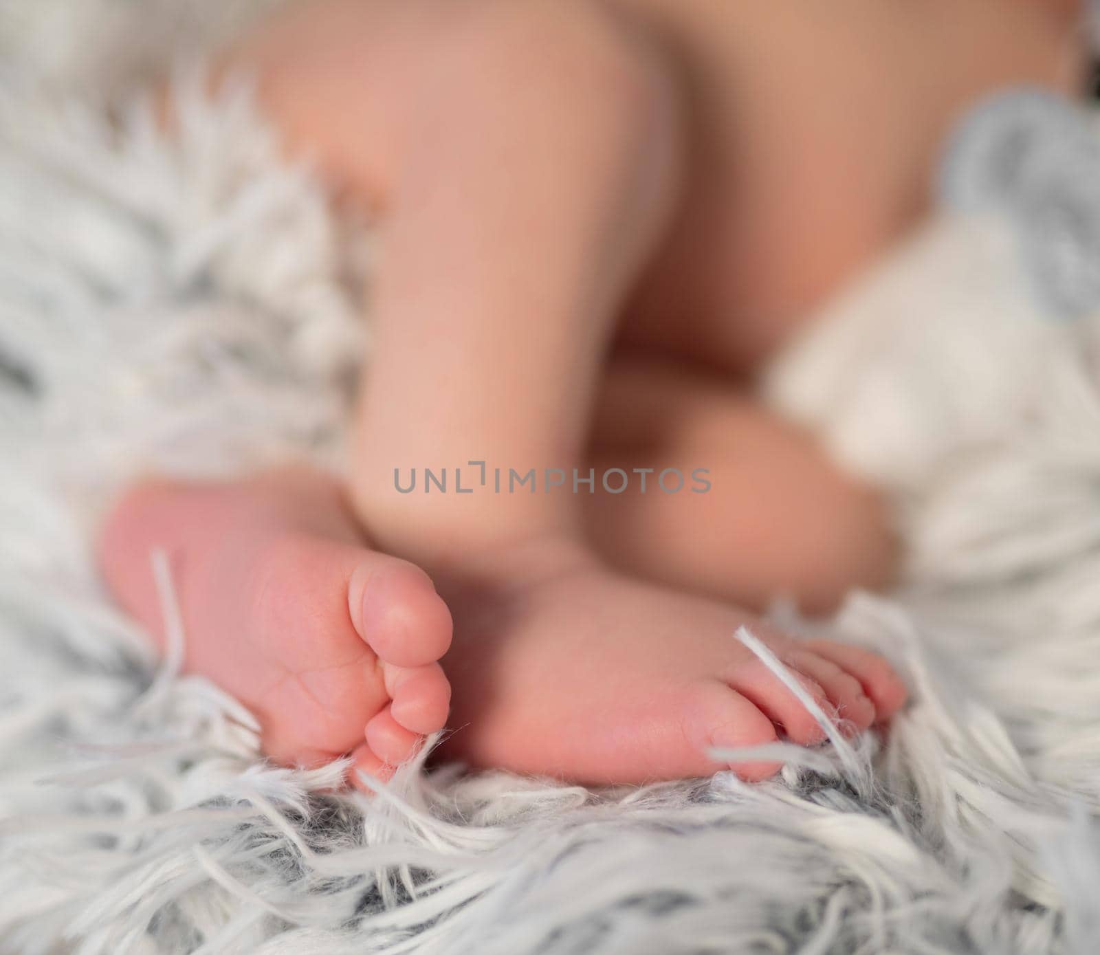 lovely folded legs of newborn baby on furry gray blanket, closeup