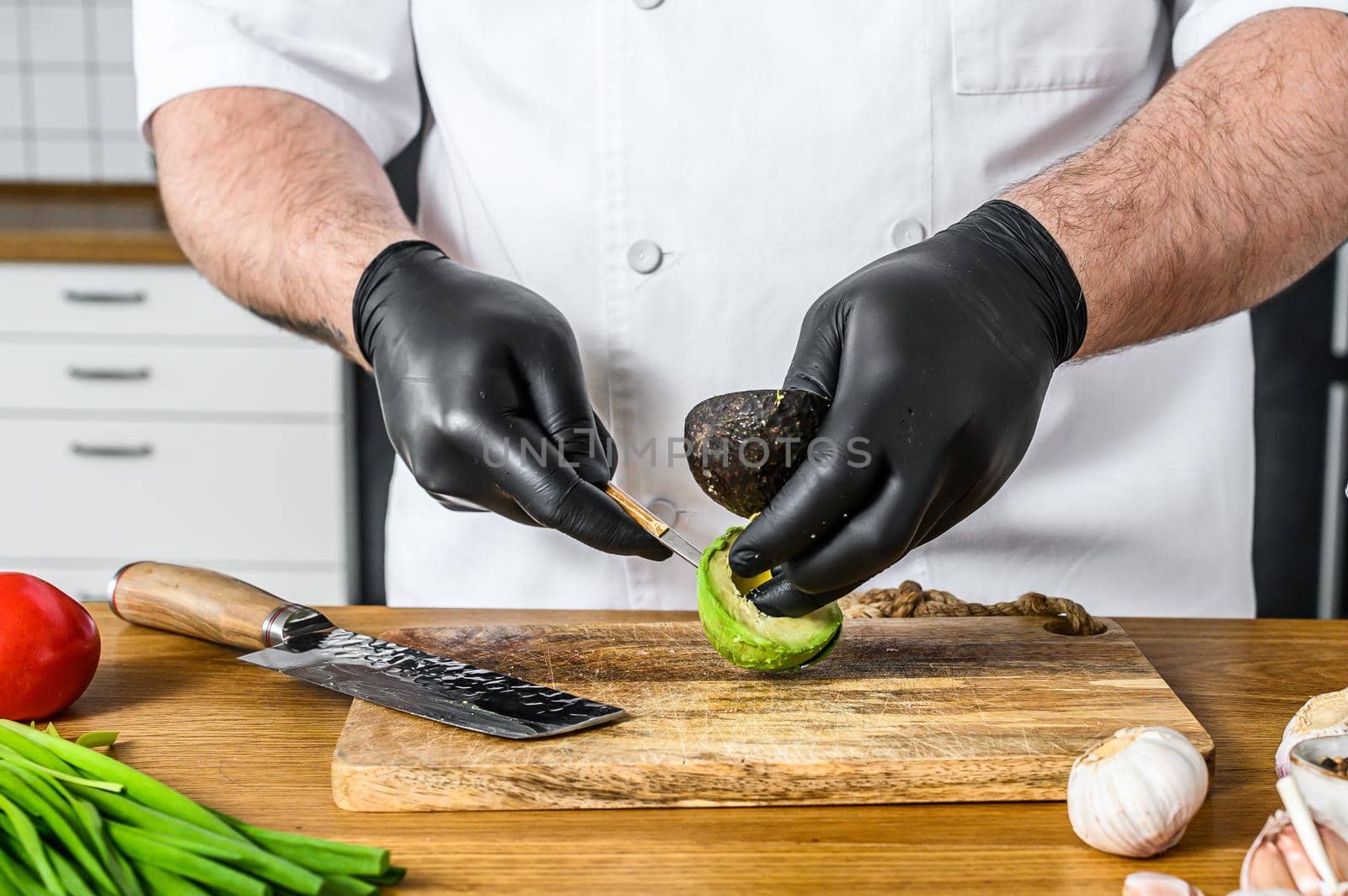 A chef in black gloves prepares guacamole from fresh avacado Hass.