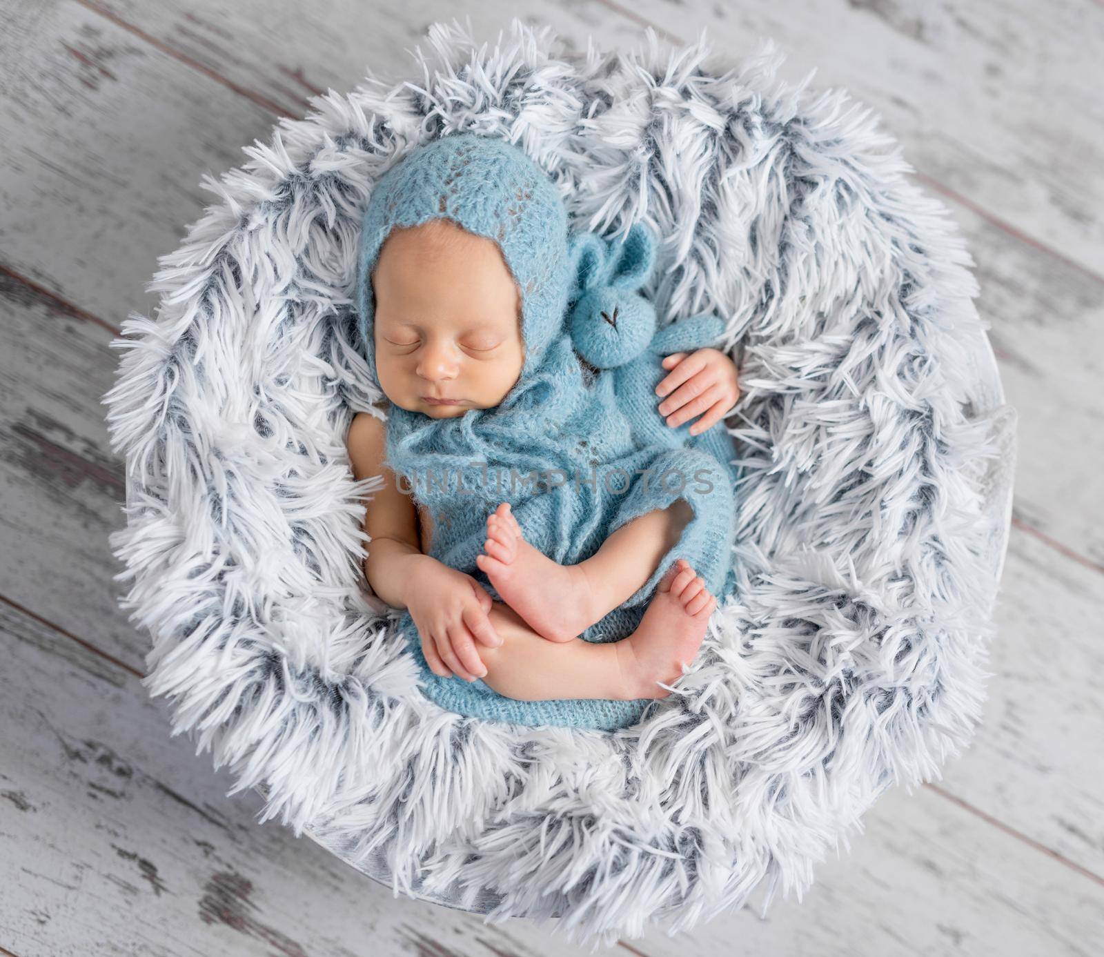 lovely infant in hat and jumpsuit sleeping on round little bed, top view