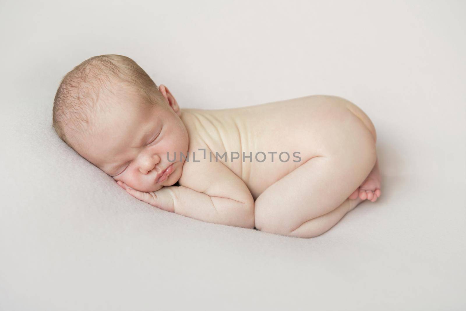 Adorable hairy naked baby napping on his belly, on a soft white blanket