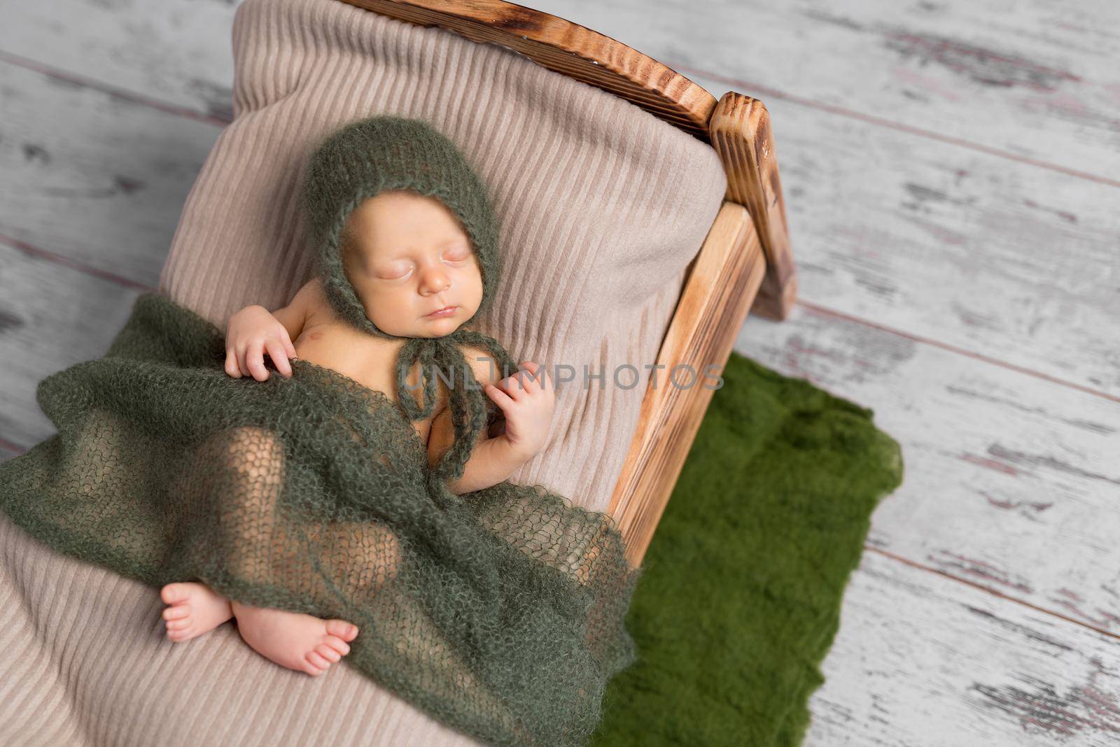 cute sleeping newborn baby in hat on little bed covered with blanket