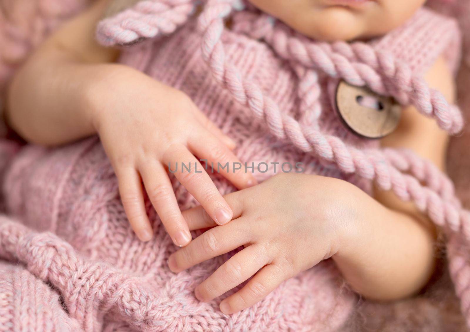 tiny newborn child hands on knitted clothes, close up