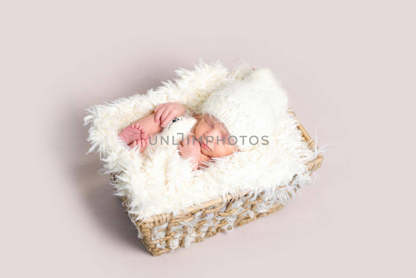 Adorable newborn baby asleep on back with legs curled up. Little baby holding plush toy while sleeping in white costume
