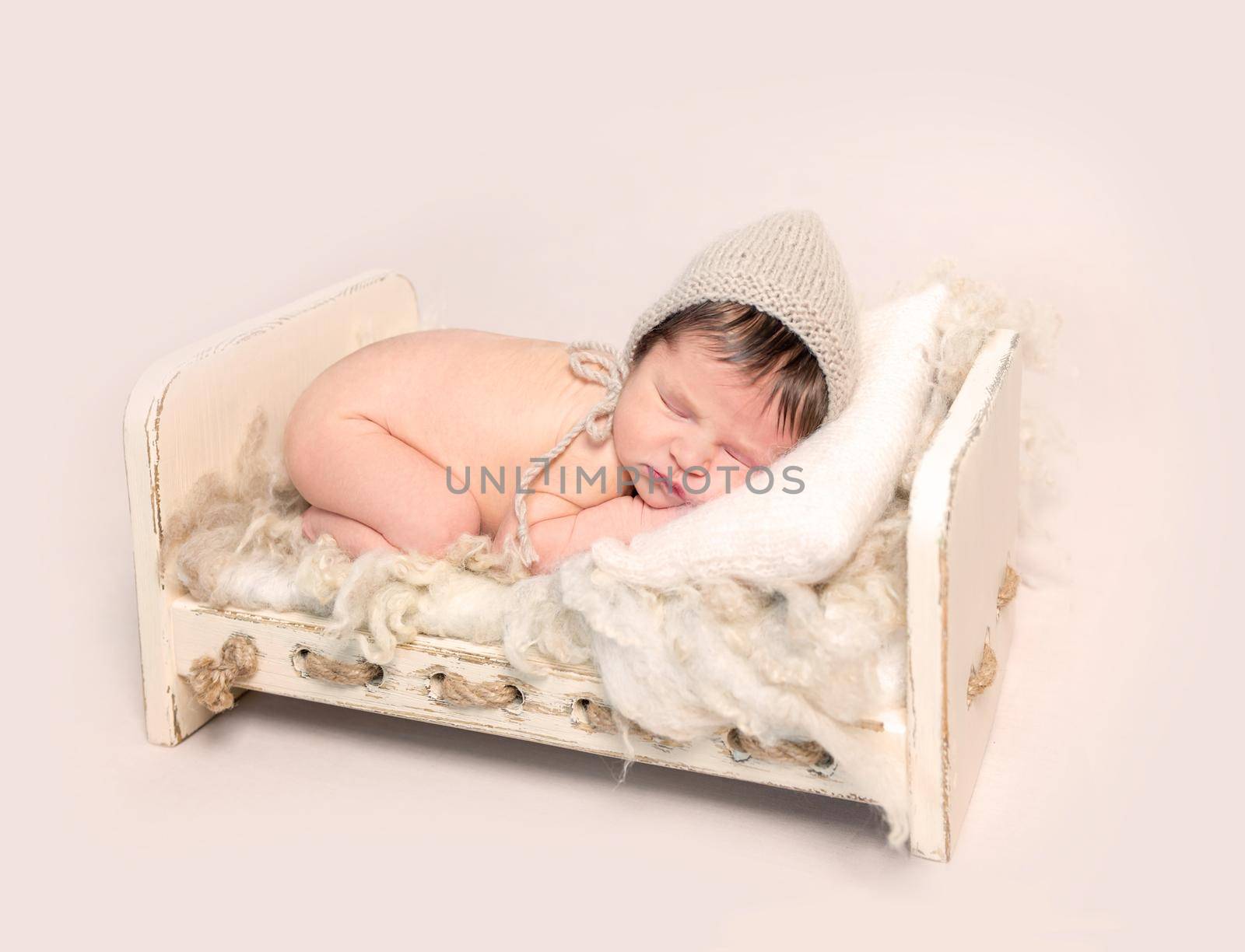 Adorable newborn baby sleeping on his stomach on wooden crib covered with furry rug