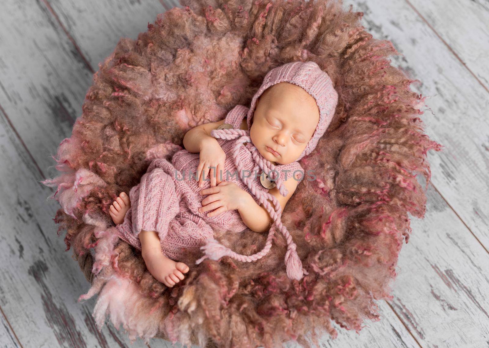 newborn baby in pink hat and jumpsuit sleeping in round bed, top view