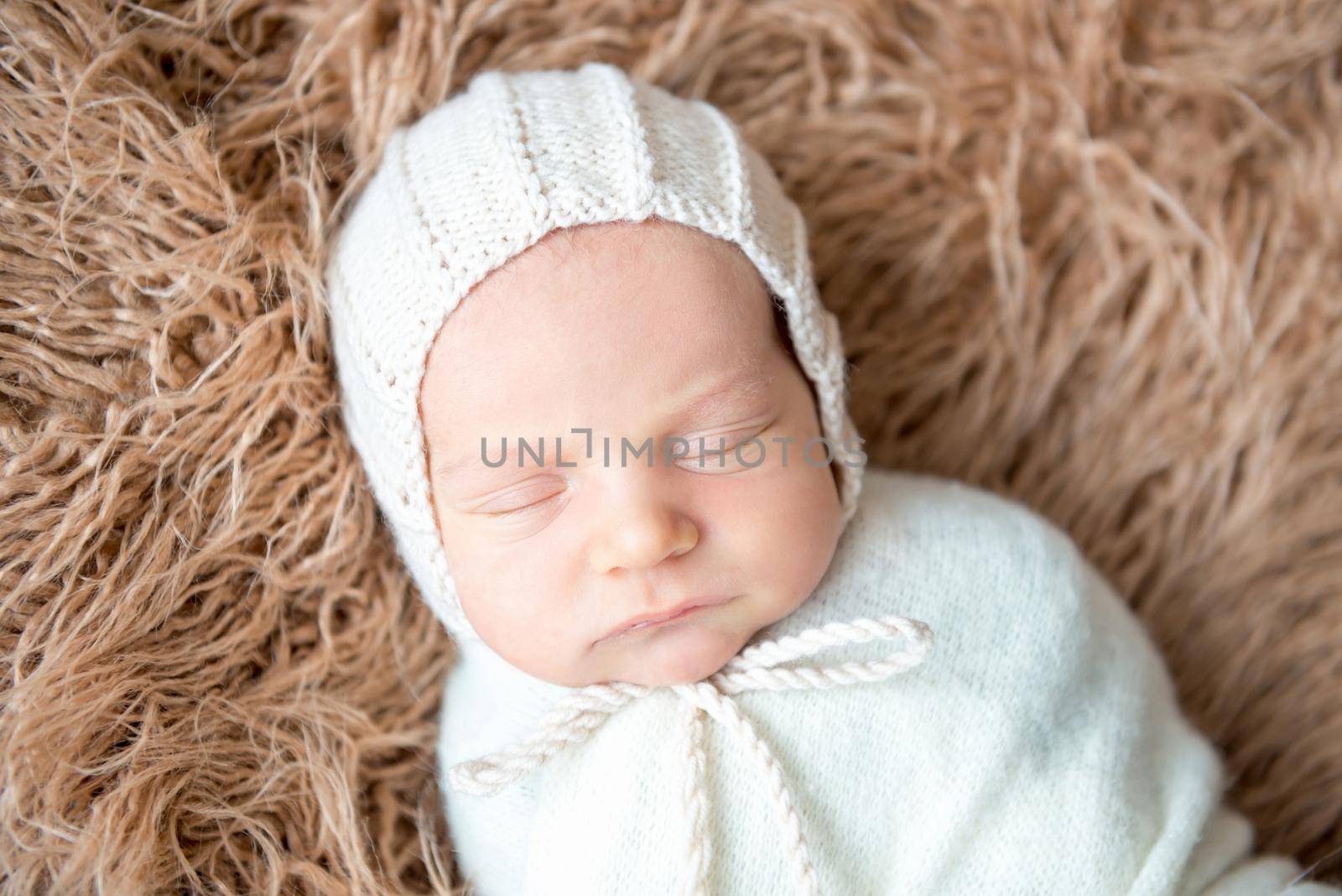 Newborn child swaddled in a white woolen cloth is sleeping on brown fluffy plaid