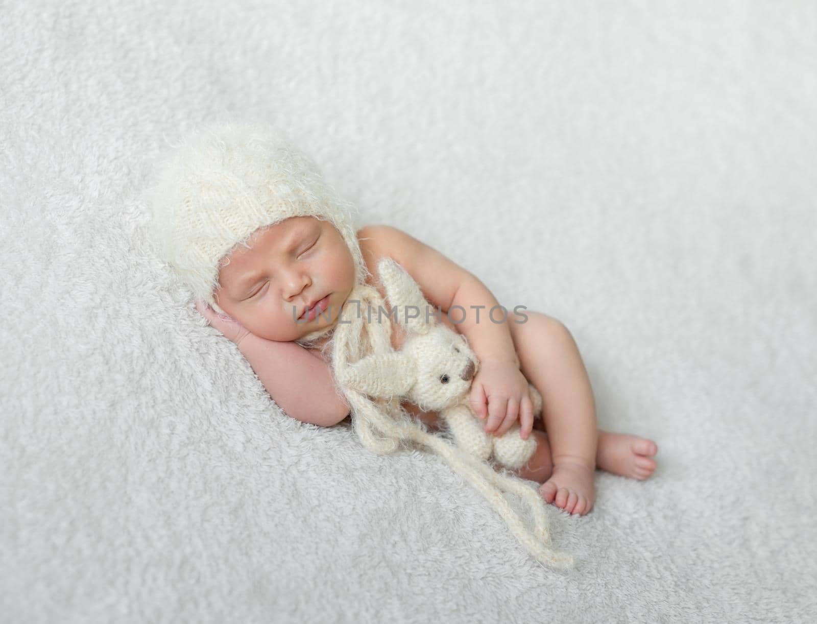 bare sleeping baby in hat with toy on white blanket by tan4ikk1