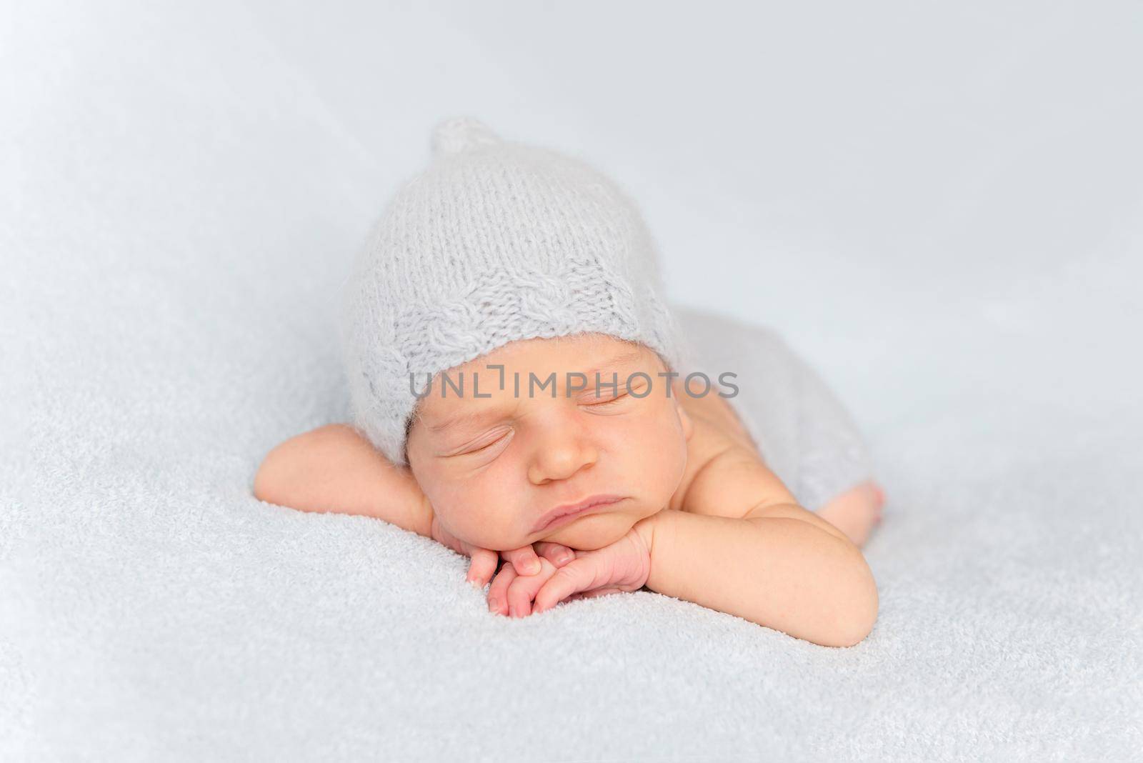 Tender little baby comfortably sleeping on belly. Newborn in tushy up pose on white blanket