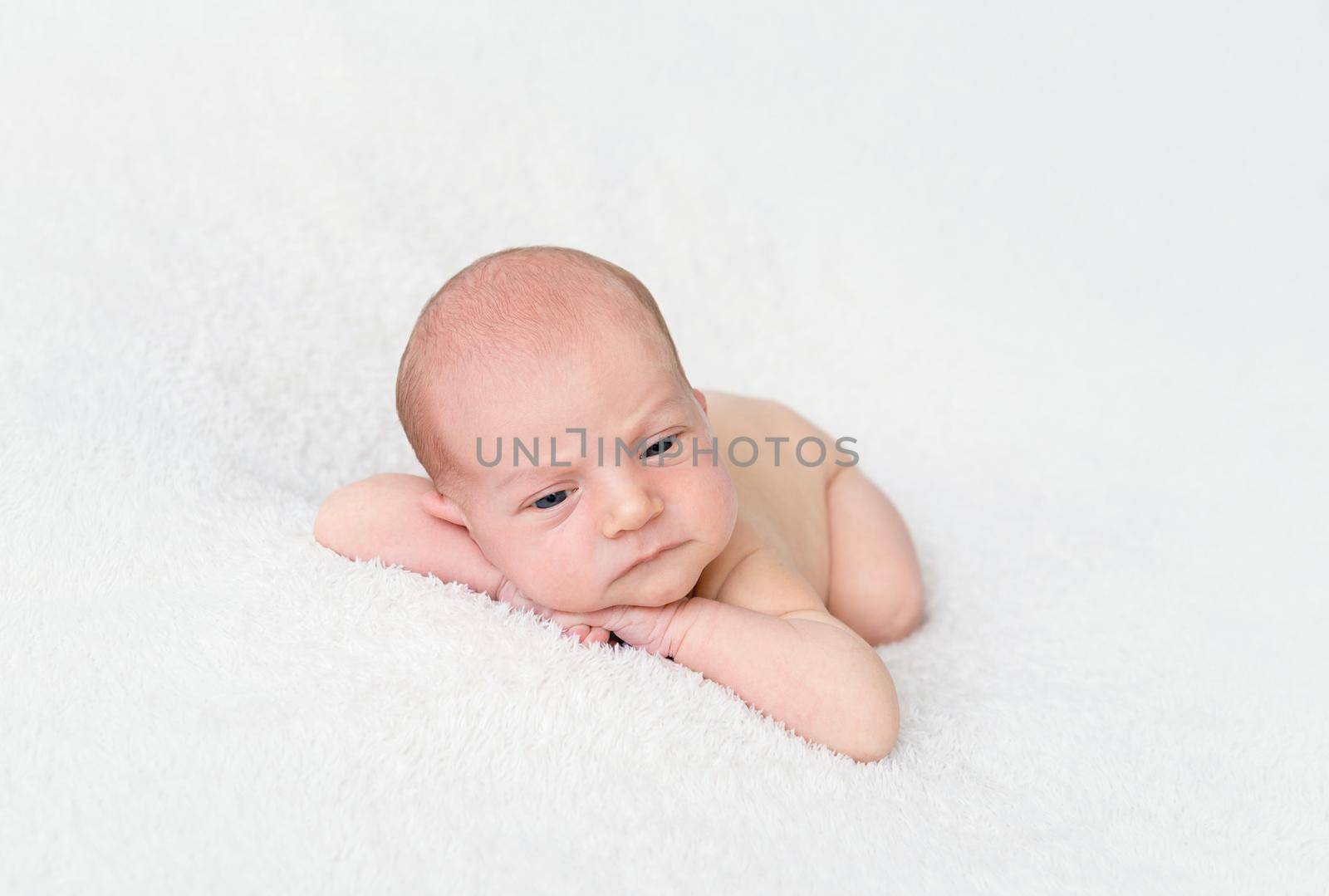 Tender newborn baby boy lying on a white blanket with his head on his hands. Newborn baby looking at camera