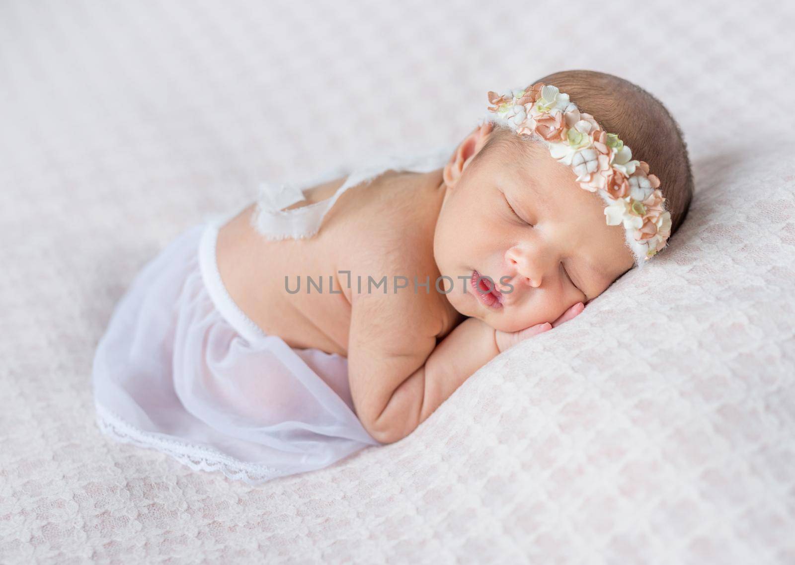 lovely newborn girl with headband sleeping on her stomach and hands under her head, covered with white shawl