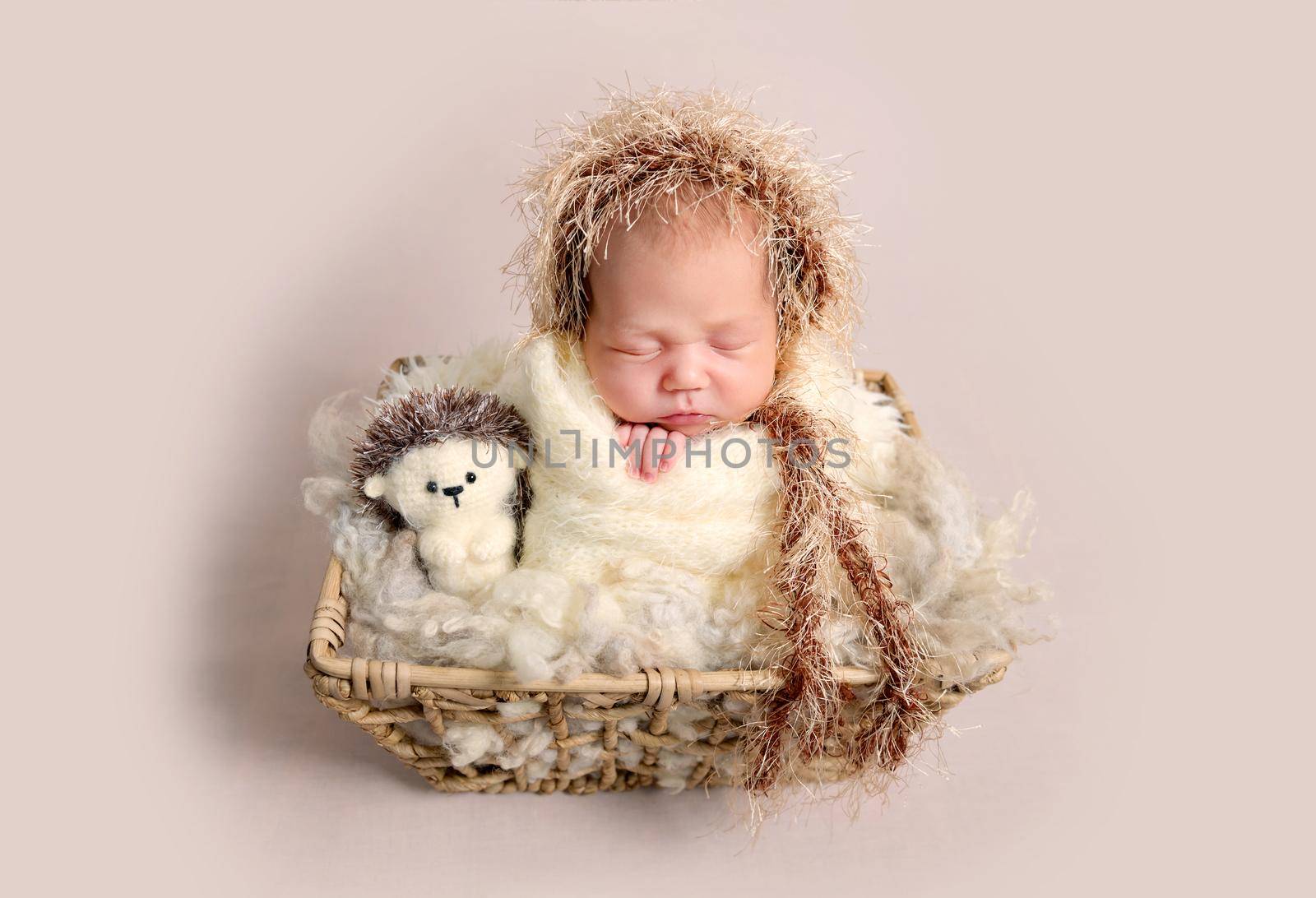 Charming little newborn baby with chubby cheeks sleeping happily in basket with soft toys. Babby wrapped in soft knitted scarf