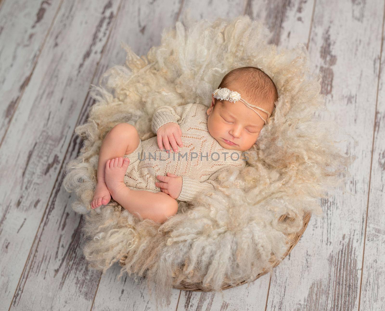 lovely sleeping newborn baby in knitted jumpsuit in basket with fluffy blanket