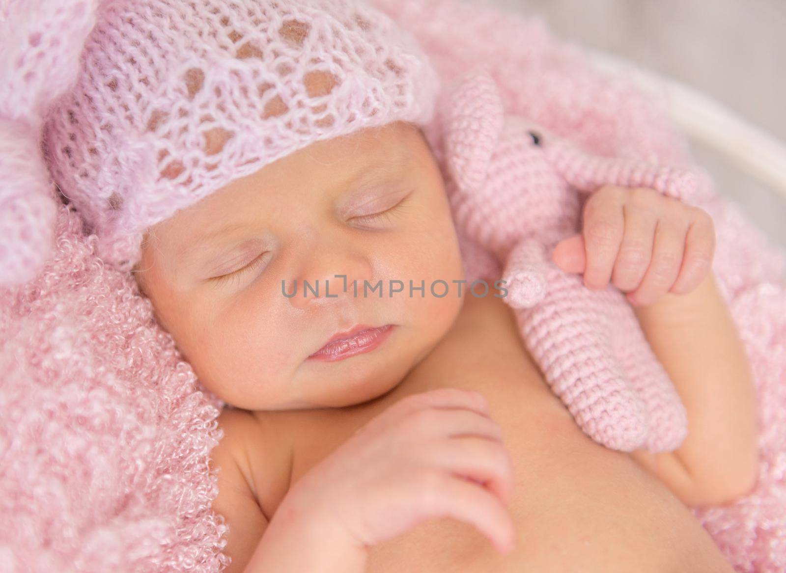 lovely newborn girl in pink panties and hat, with toy in basket on wooden background, top view