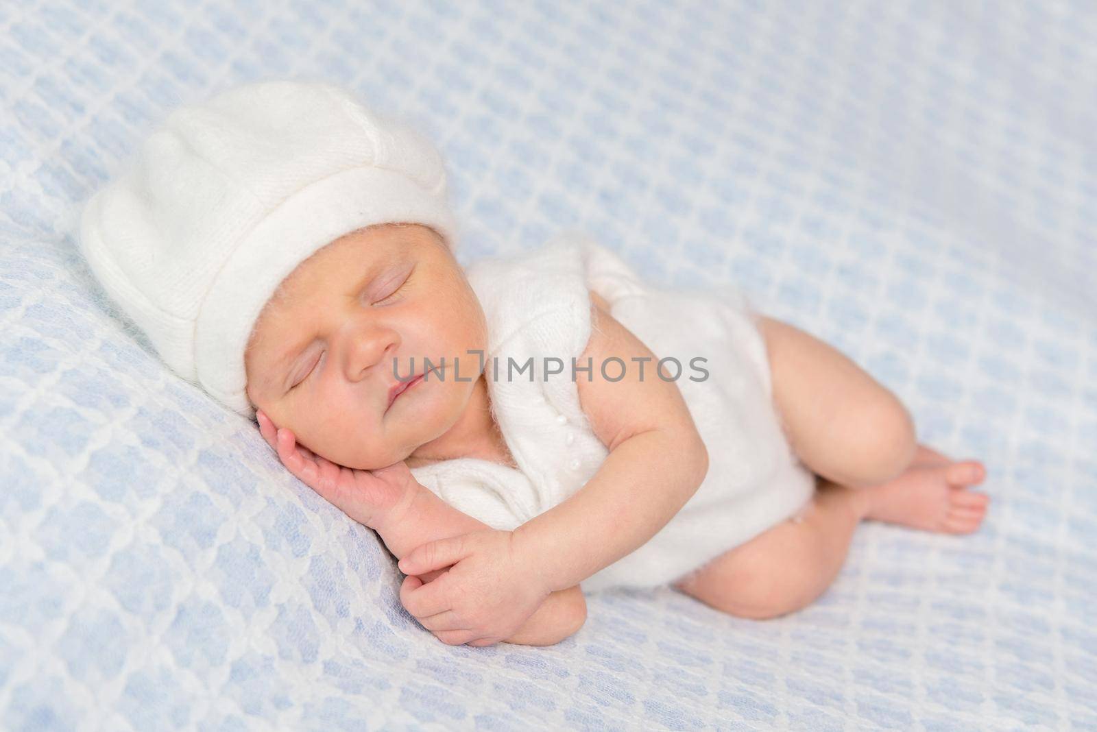 cute sleeping on hand newborn in white romper and hat on a blanket