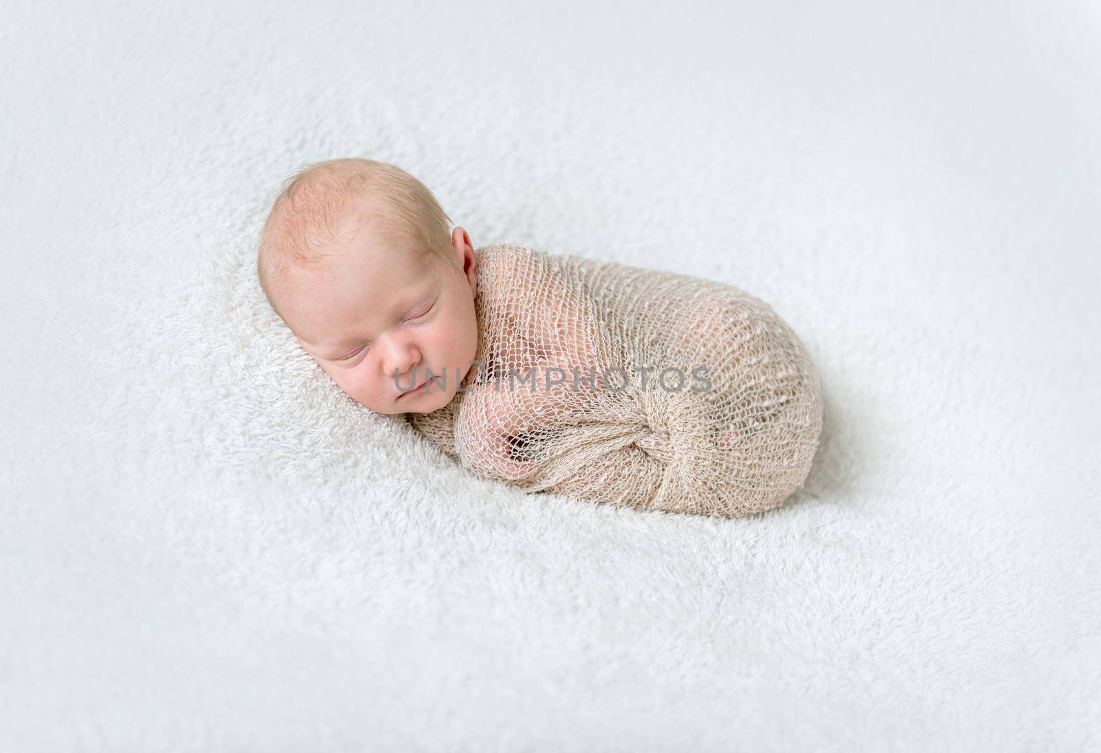 lovely sleeping baby wrapped in beige diaper on white blanket