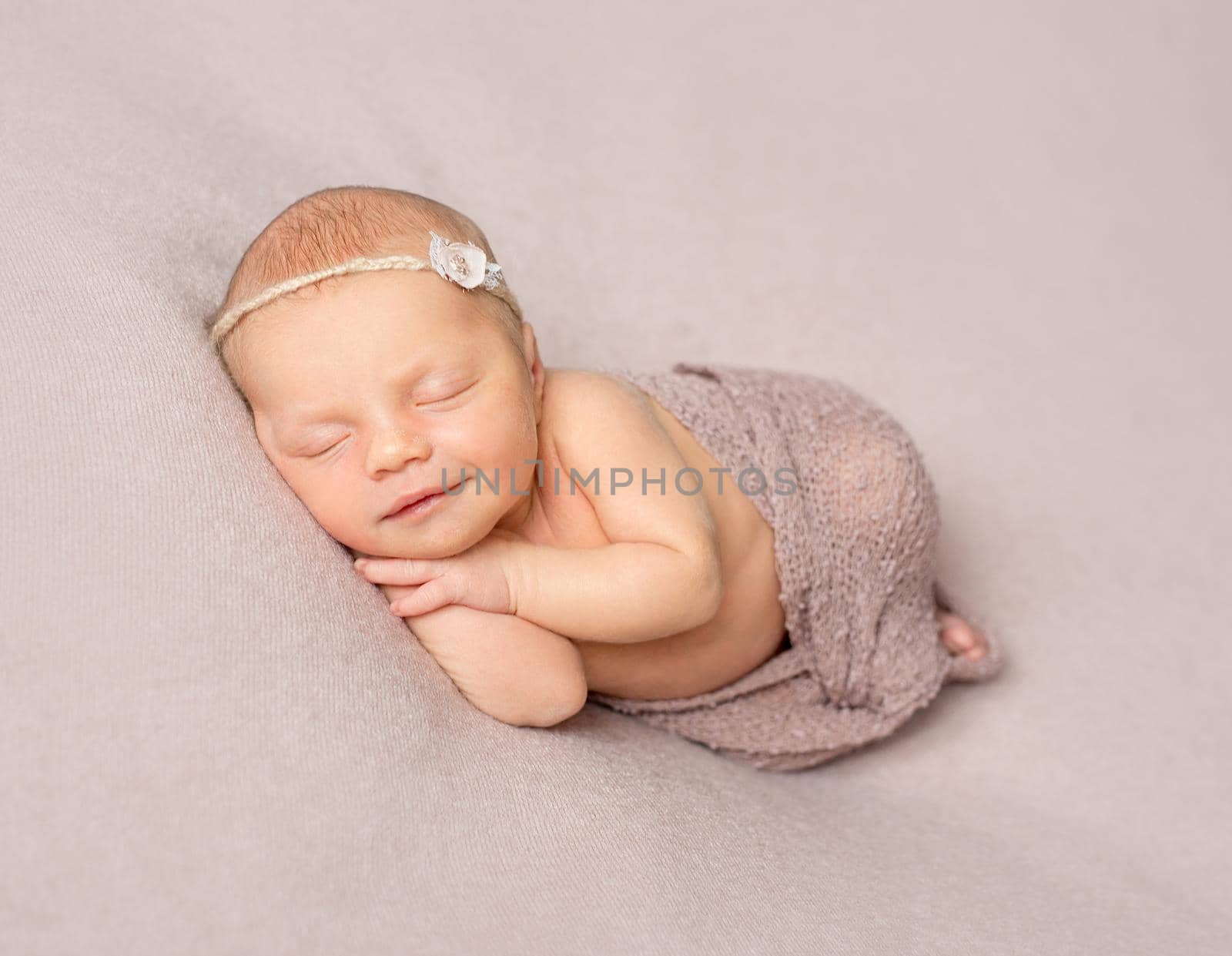 smiling sleeping newborn girl with hands under her head covered with knitted shawl