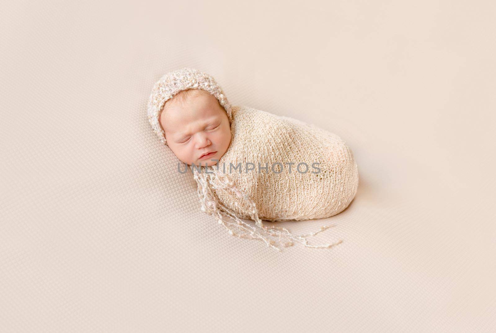 lovely wrapped baby in hat sleeping on a beige blanket by tan4ikk1