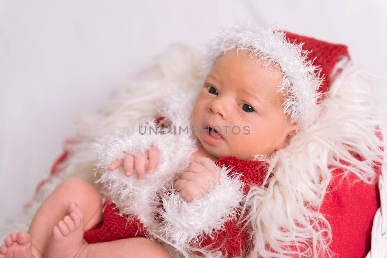 Lovely infant dressed as a Santa Claus lying on a soft red fluffy pillow