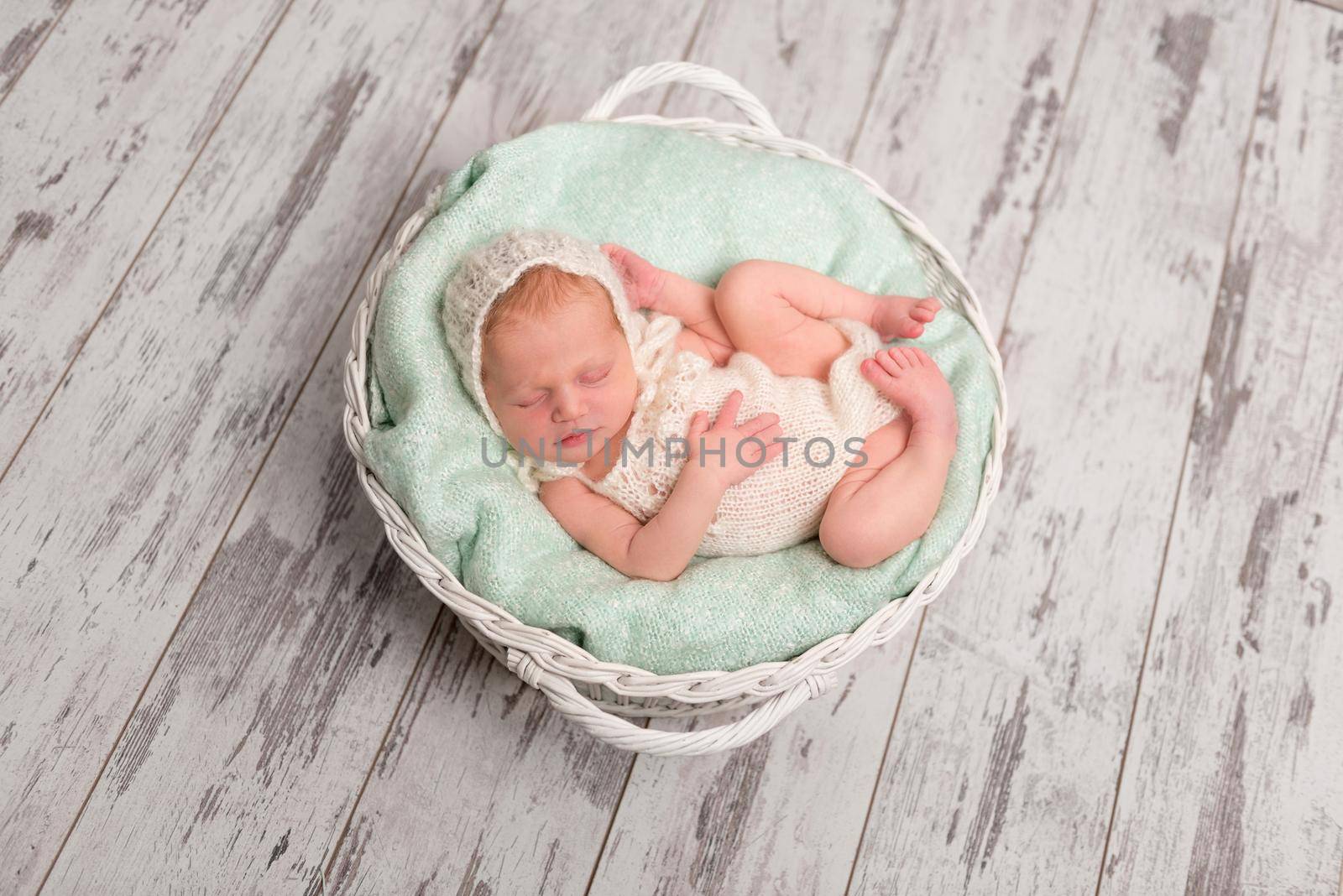 lovely newborn baby in hat and jumper sleeping in basket