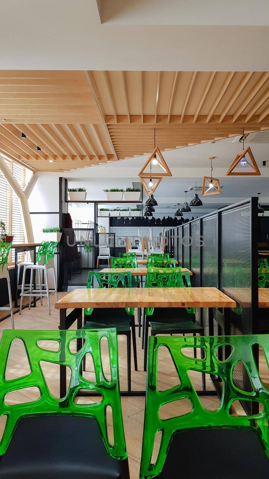 Cafeteria, no people dining room with wooden tables and green chairs. Interior with wood and metal elements. Modern dining areas with window lighting. Ukraine, Kiev - February 19, 2021.