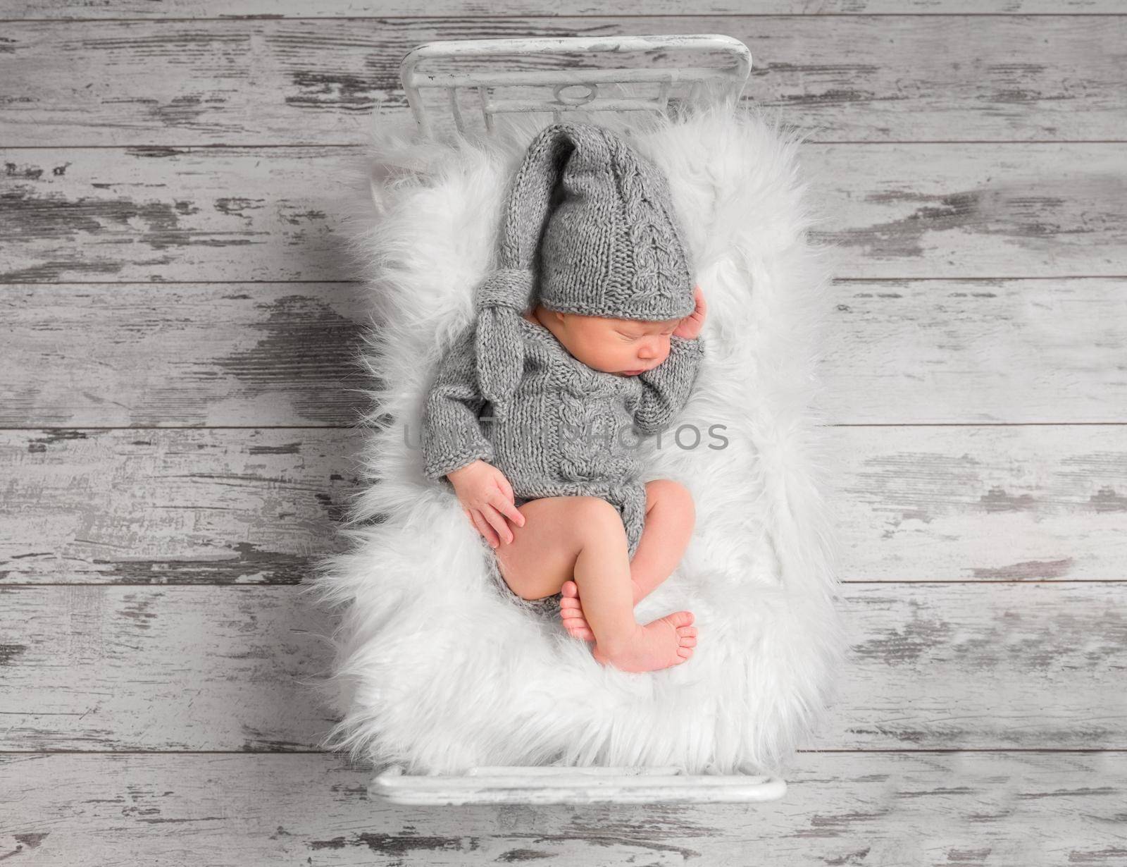 Lovely infant in a knitted gray suit sleeping in a comfortable bed, topview