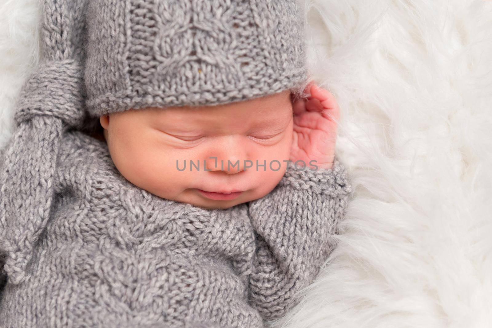 Sweet child in a hat napping all enveloped with a gray blanket, closeup