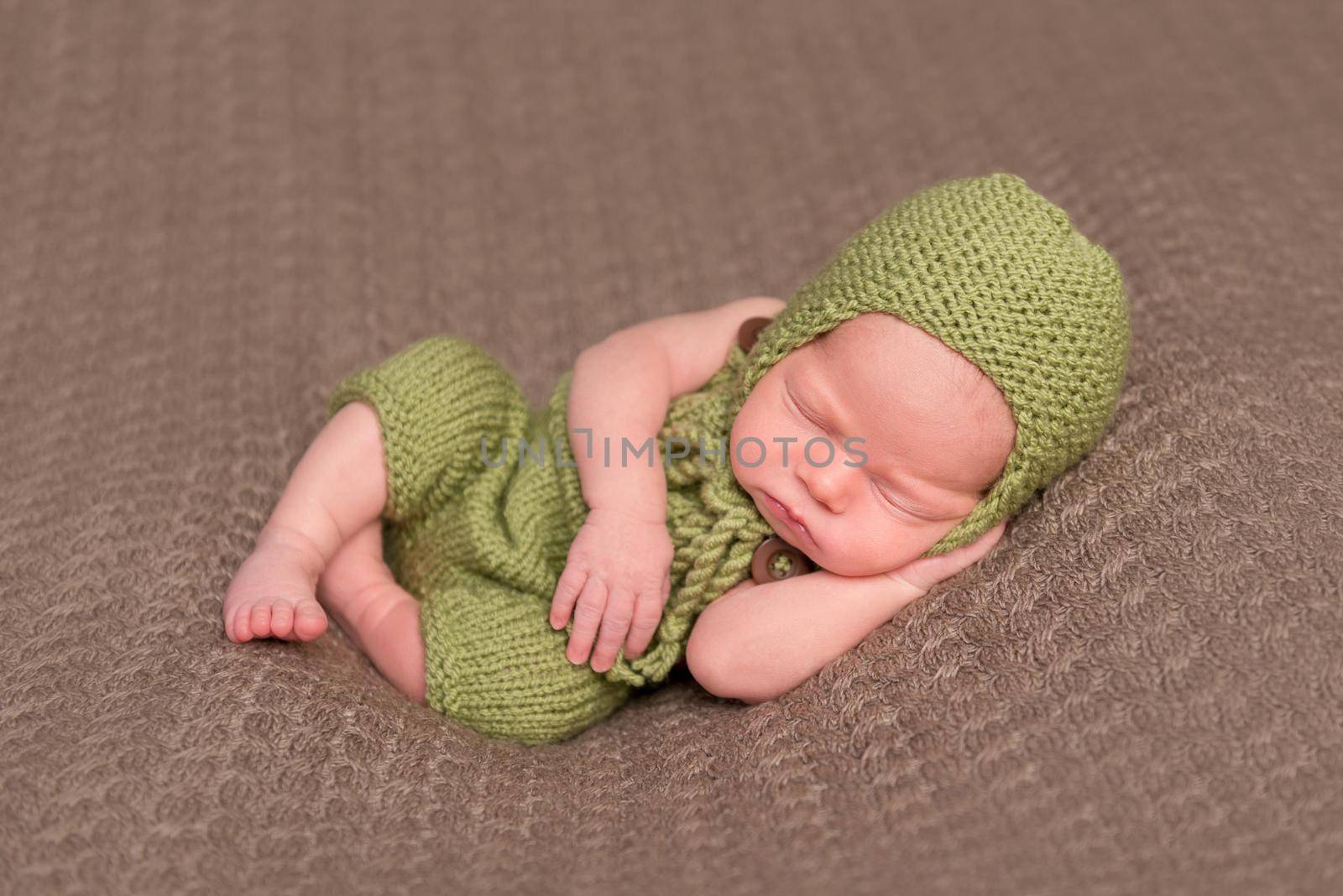 Cute newborn in a knitted green hat sleeping on a soft blanket