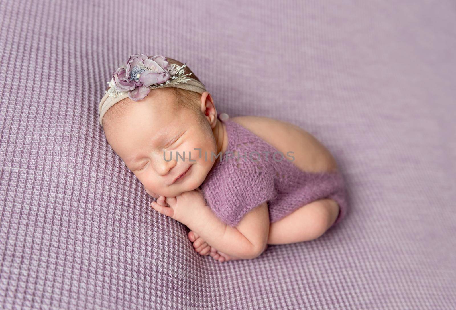 Little newborn baby girl in purple bodysuit smiling while sleeping by tan4ikk1