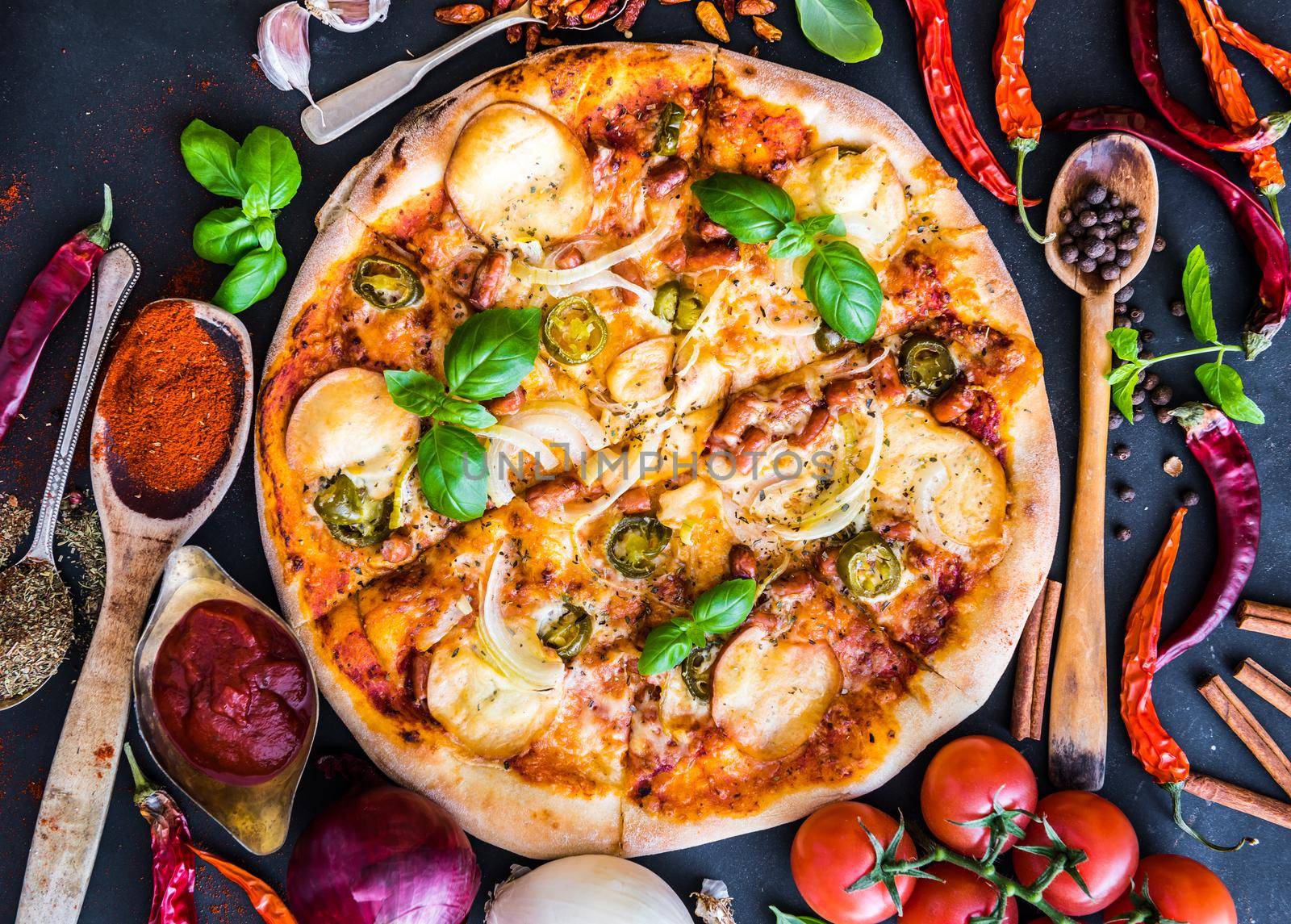 tasty pizza on a black background with spices and vegetables