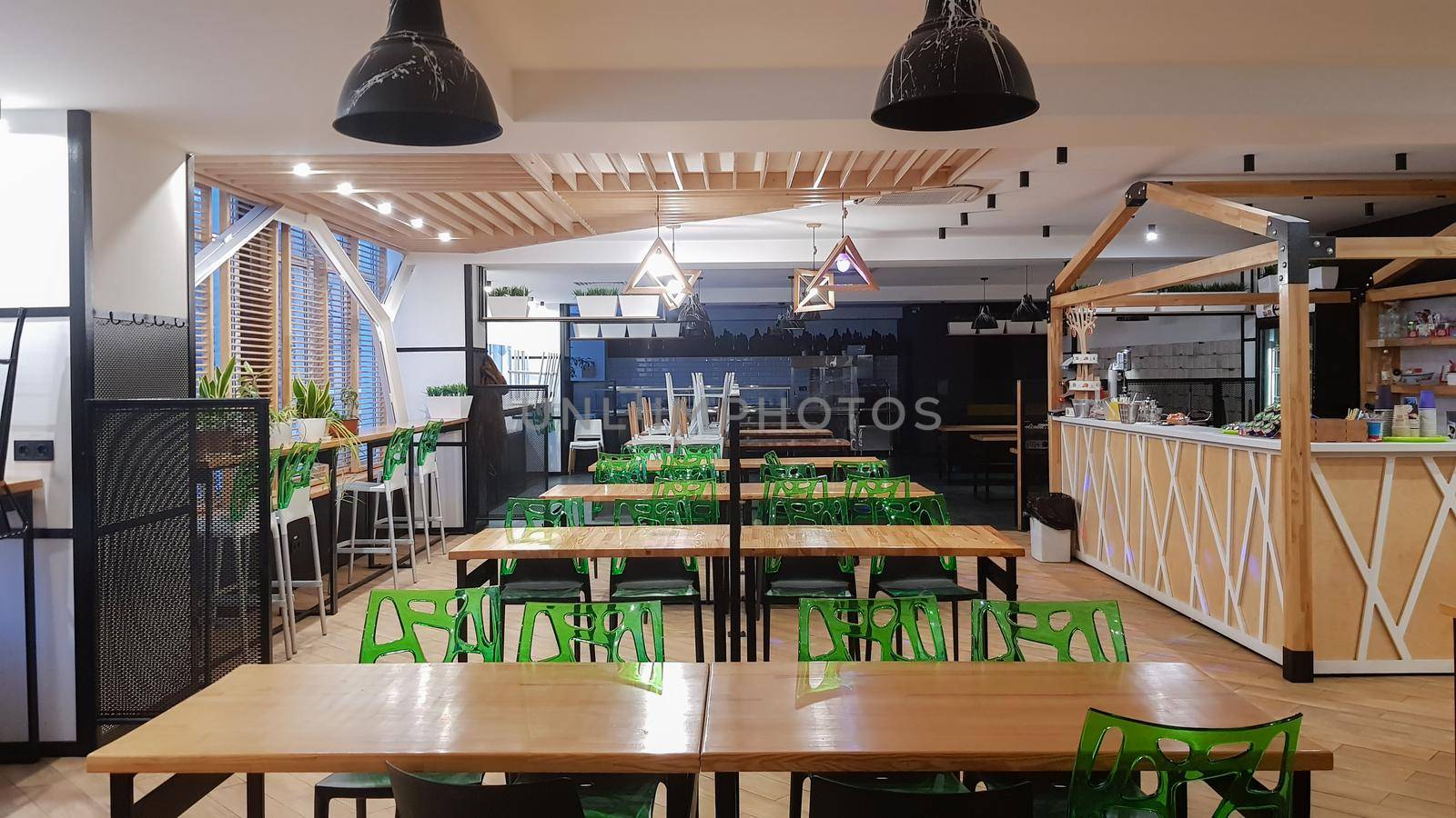 Cafeteria, no people dining room with wooden tables and green chairs. Interior with wood and metal elements. Modern dining areas with window lighting. Ukraine, Kiev - February 19, 2021.