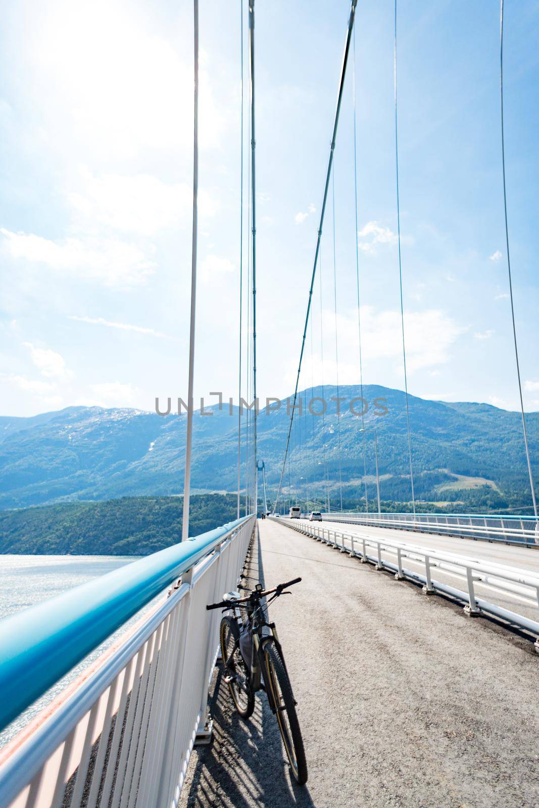 Theme of mountain biking in Scandinavia. human tourist in helmet and sportswear on bicycle in Norway on Hardanger Bridge suspension bridge thrown across the Hardanger Fjord in southwestern Norway by Tomashevska