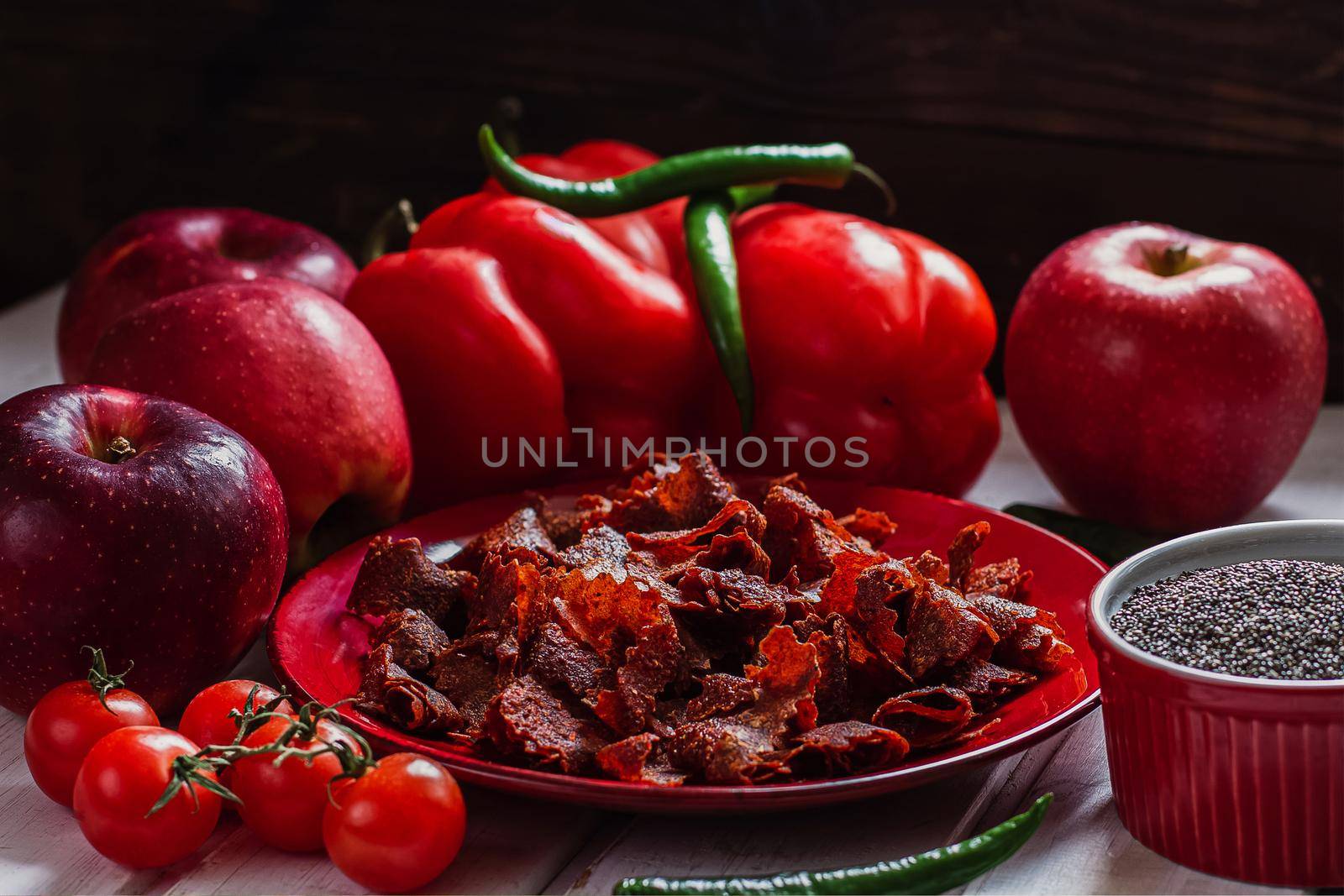 Sun-dried tomatoes with paprikas and chilly peppers on red plate.