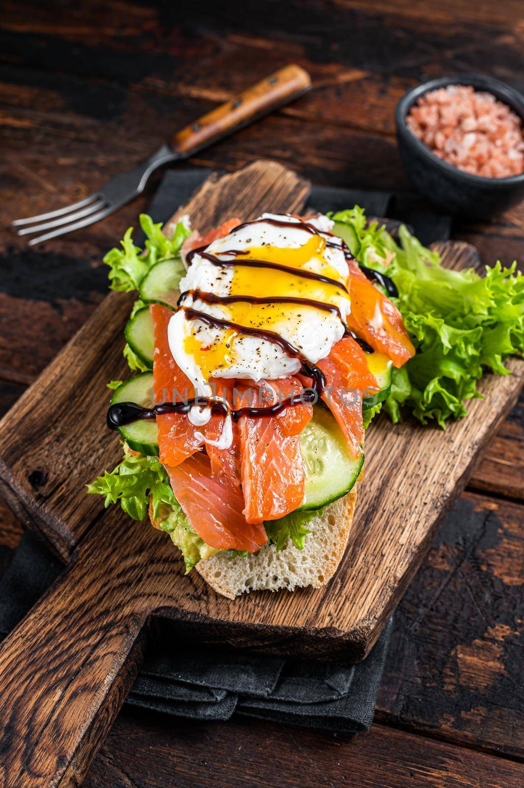 Smoked salmon Sandwich with Benedict egg and avocado on bread. Dark wooden background. Top view by Composter