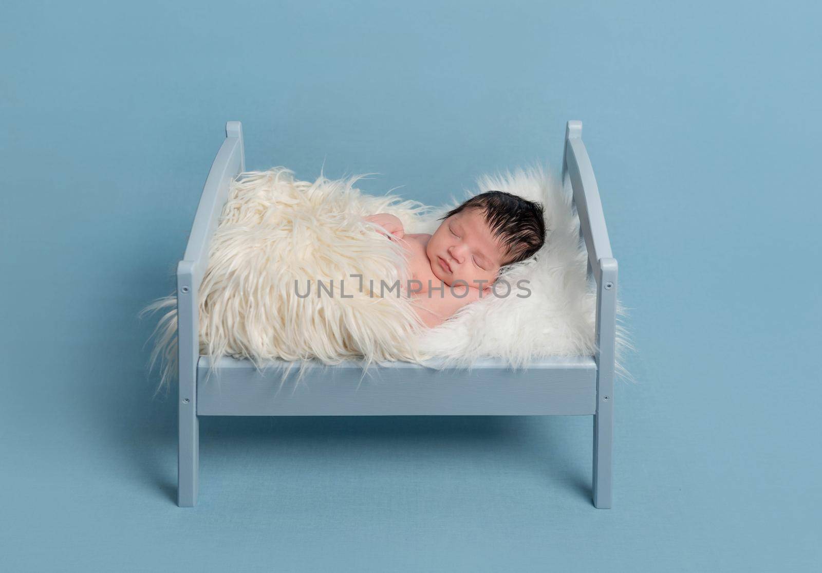 Lovely hairy newborn sleeping on a tiny bed, covered with a sofr furry blanket