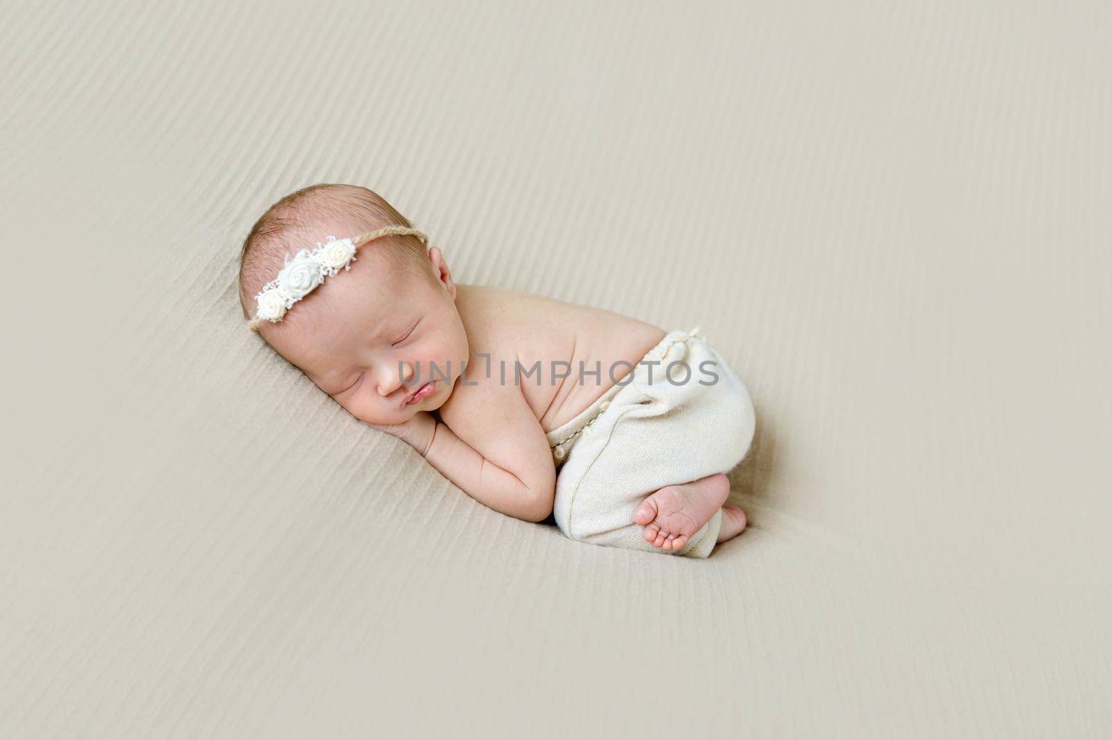 Aodrable newborn girl in hairband with flowers, sleeping on her side, funny pose