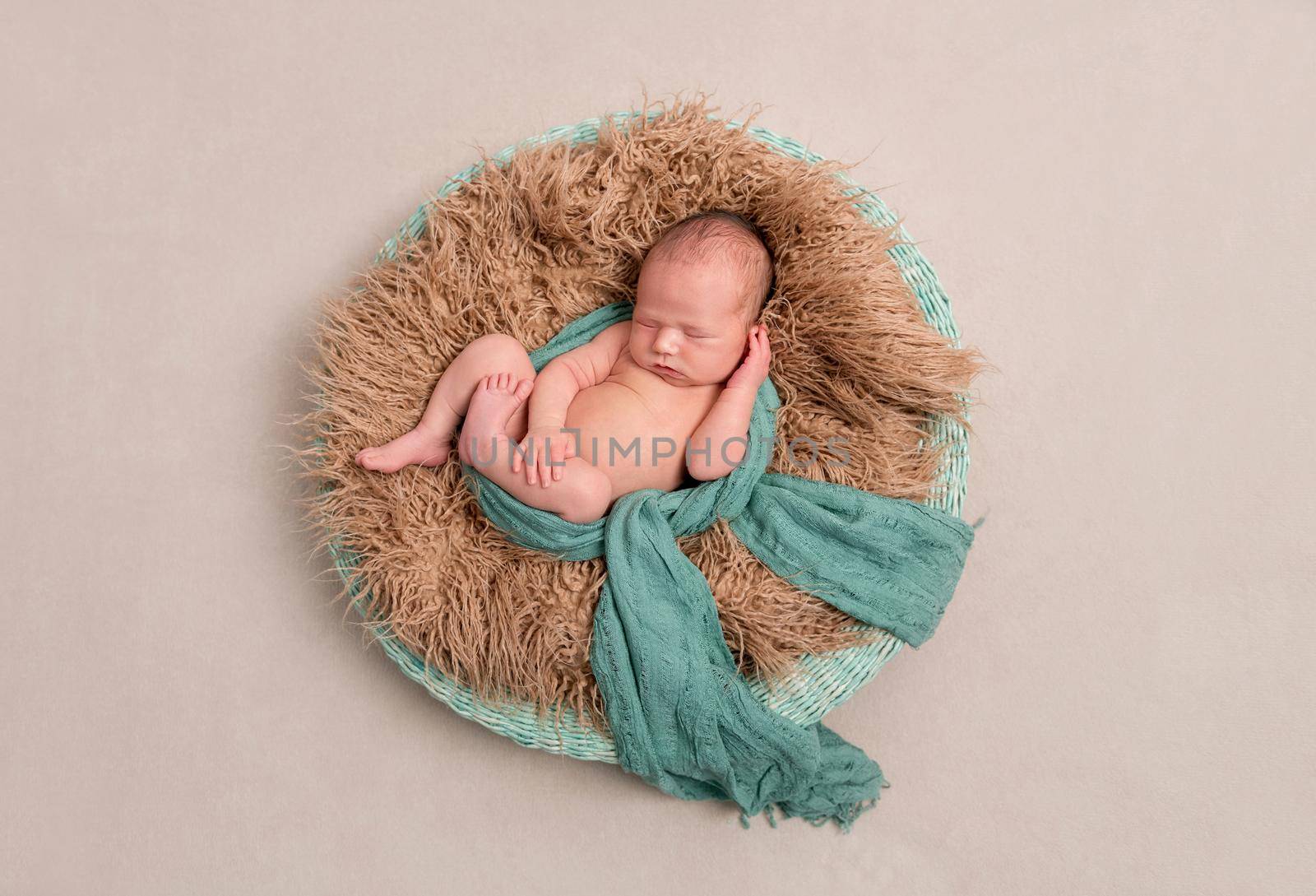 Newborn napping in a basket, enveloped with a light green scarf, topview