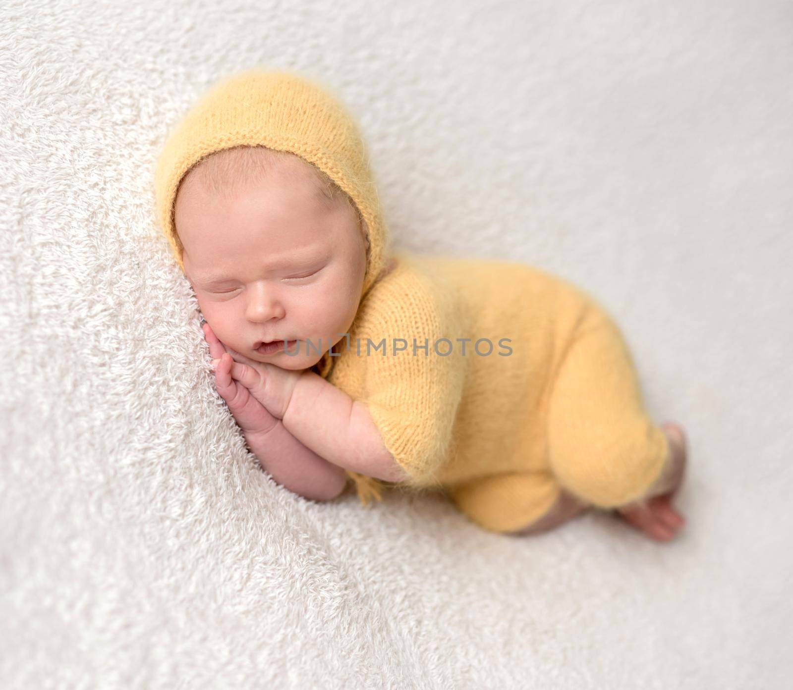Little baby weared in cute yellow knitted suit sweetly sleeping on the white soft bedcover
