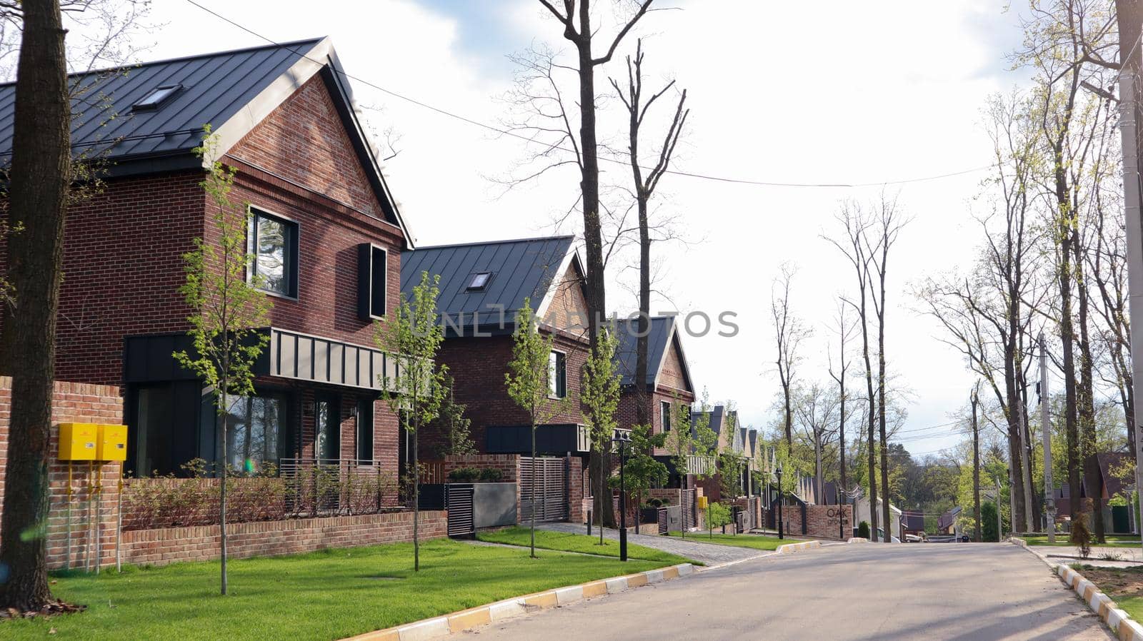 A street with houses and manicured lawns in a typical suburb. Frame made of small brown brick American country houses. Ukraine, Irpin - 07 June 2021