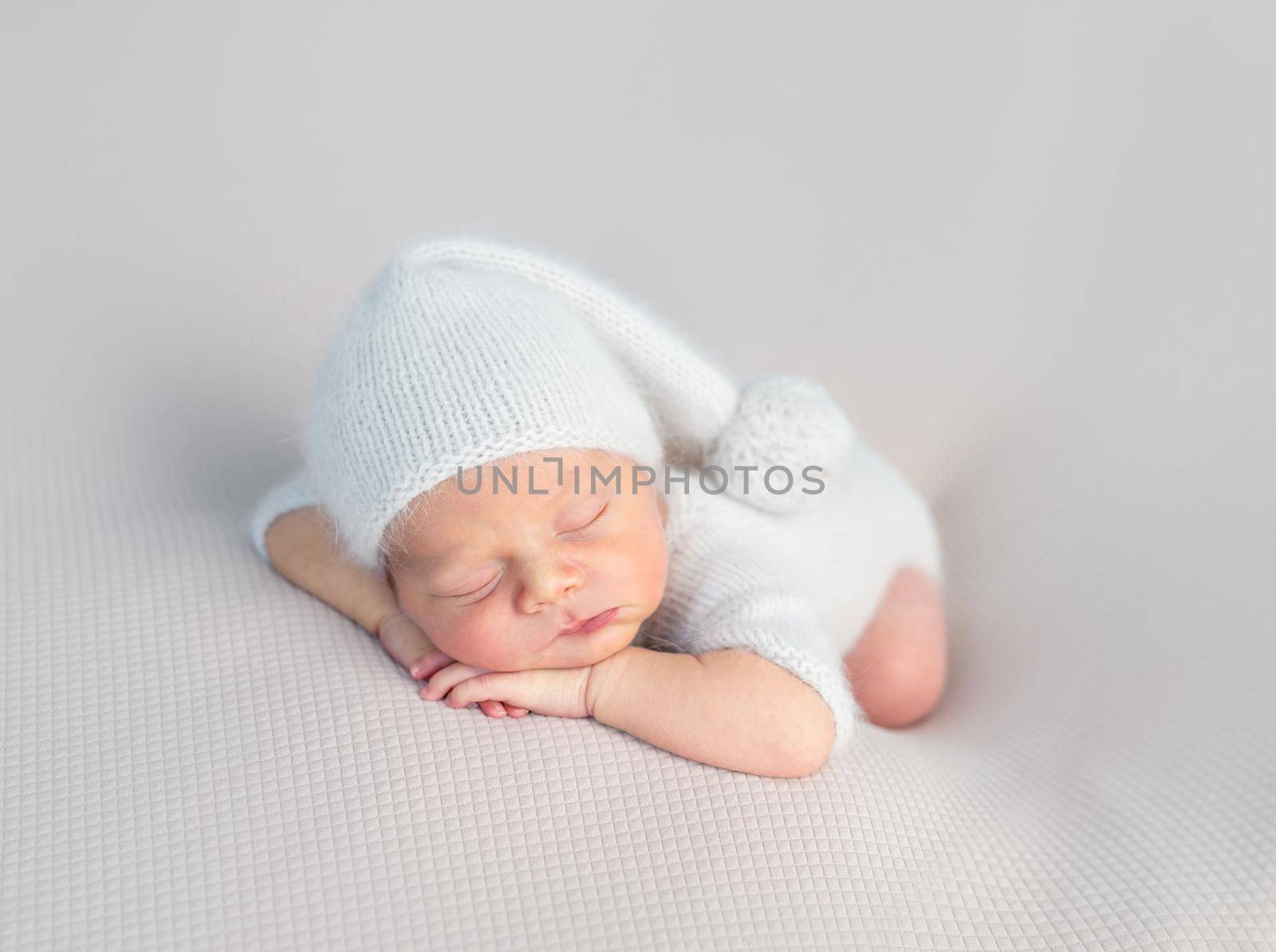 Cute little baby in white hat and knitted suit sweetly sleeping