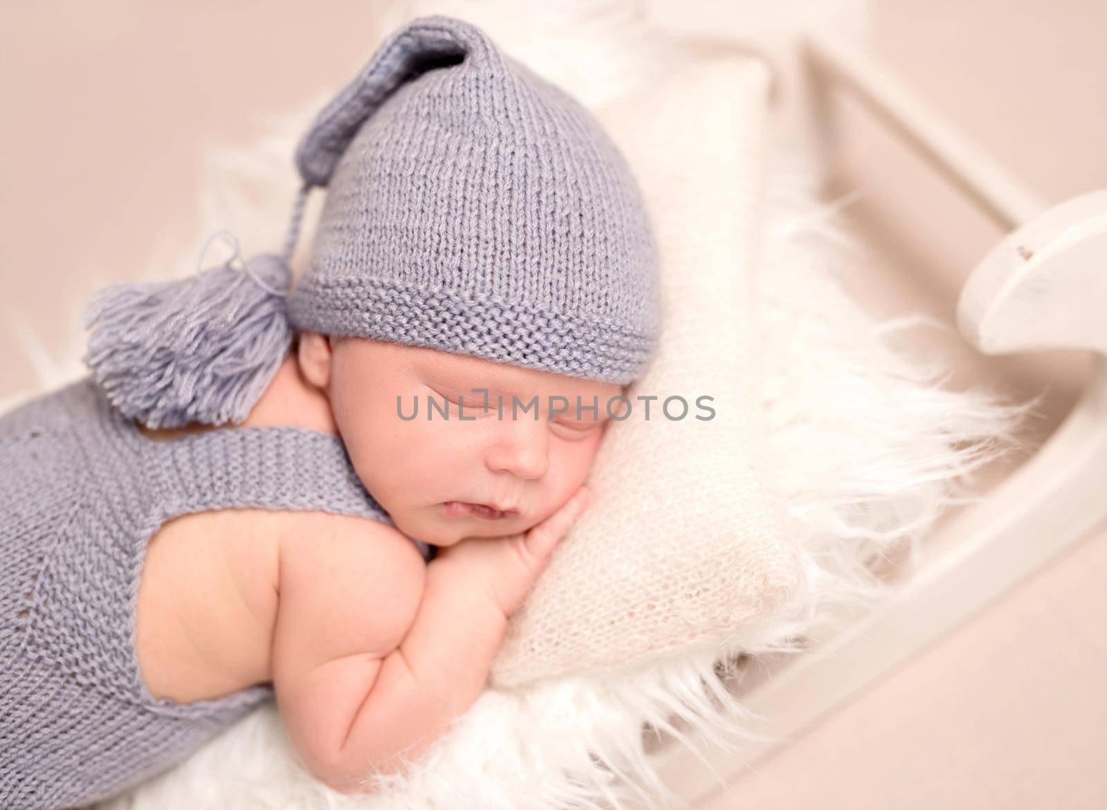 Little baby weared in light blue knitted beanie and suit sweetly sleeping on the white sleight covered with soft white coverlet , on the light pink background