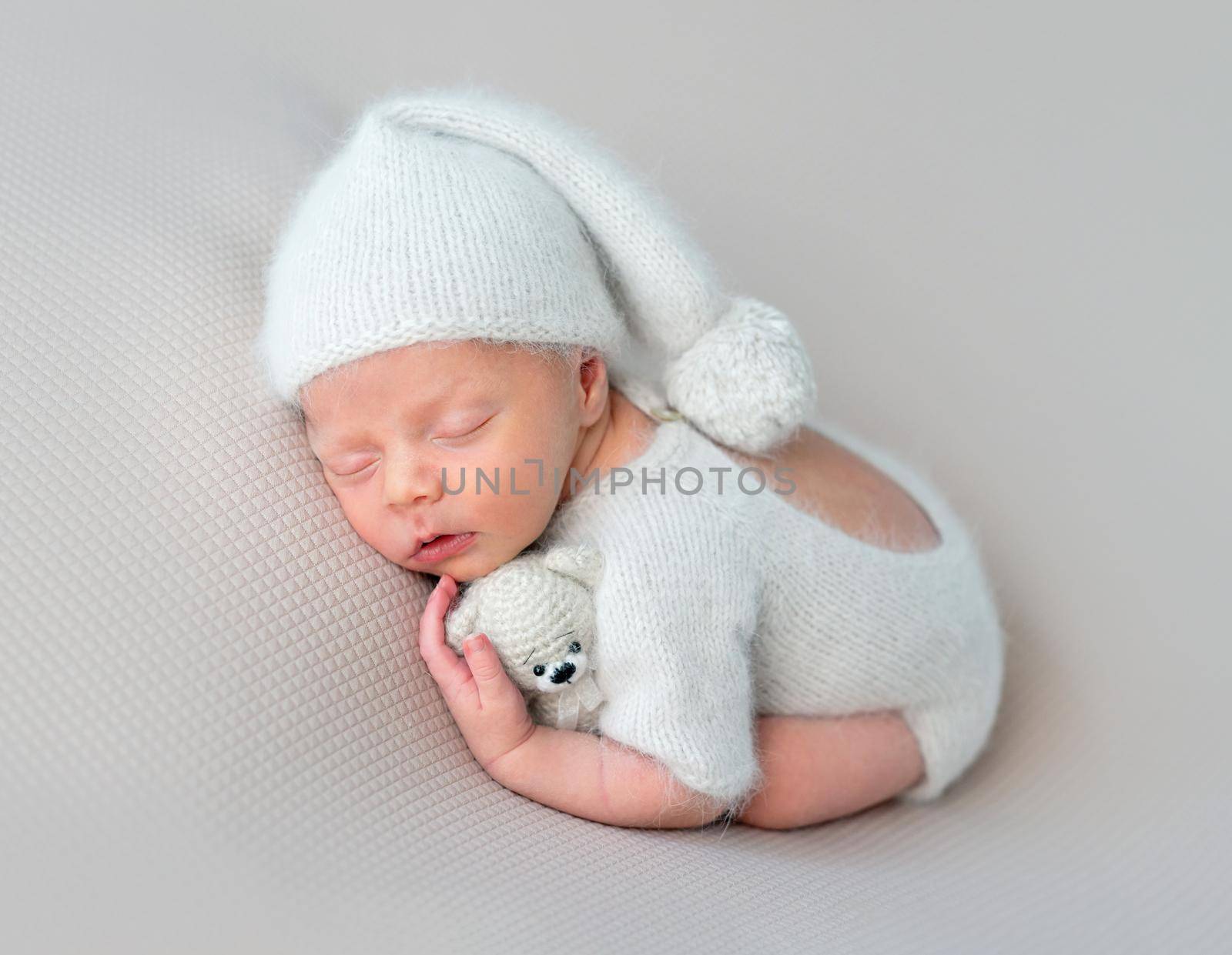 Cute little baby in white hat and knitted suit with toy sweetly sleeping