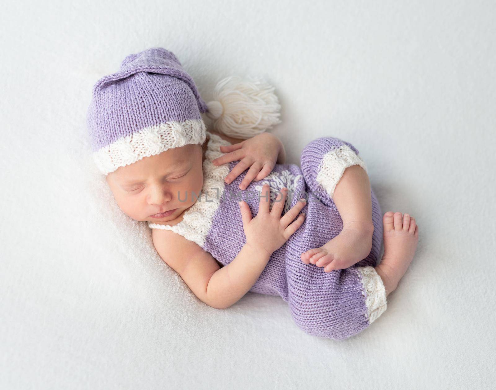 Cute little baby in white and purple knitted suit sweetly sleeping on white blanket