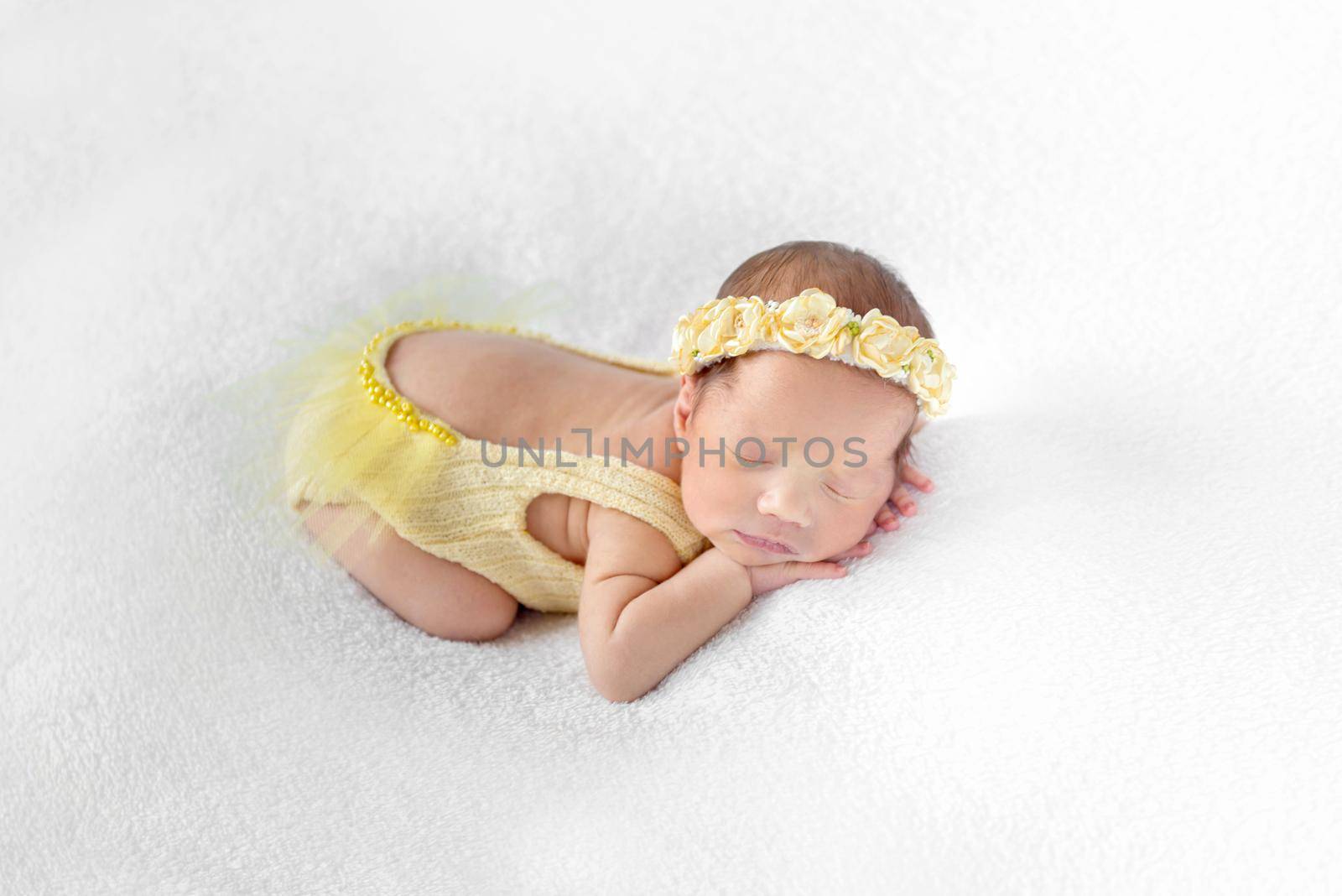 Lovely baby dressed in a yellow outfit with lowcut back sleeping on a white surface