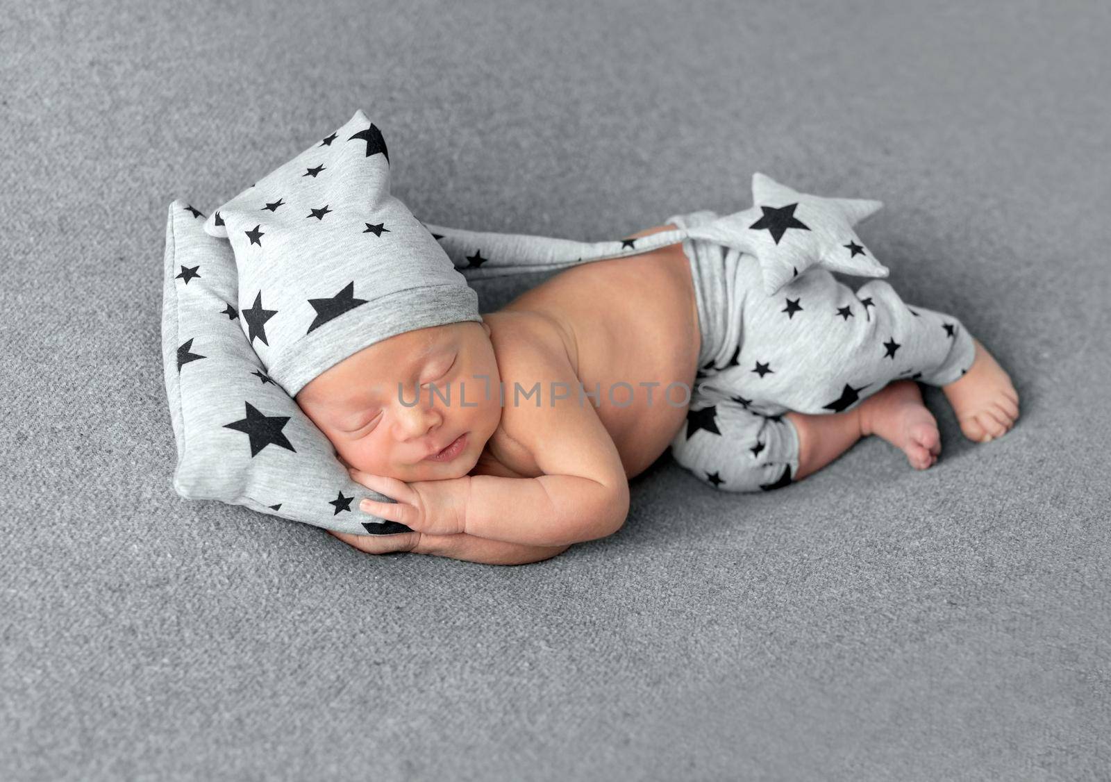 Cute little baby in hat and pants with stars pattern sweetly sleeping on gray blanket
