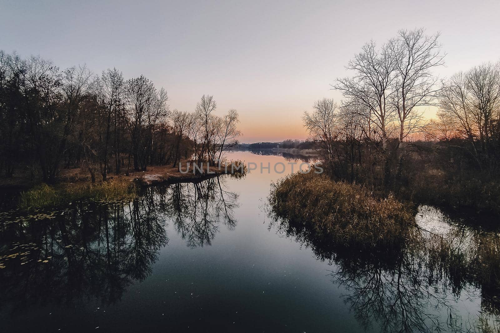 Vivid autumn sunset. Autumn landscape of sunset over river with shining grass on shore. Scenic nature at bright evening with colorful sky.