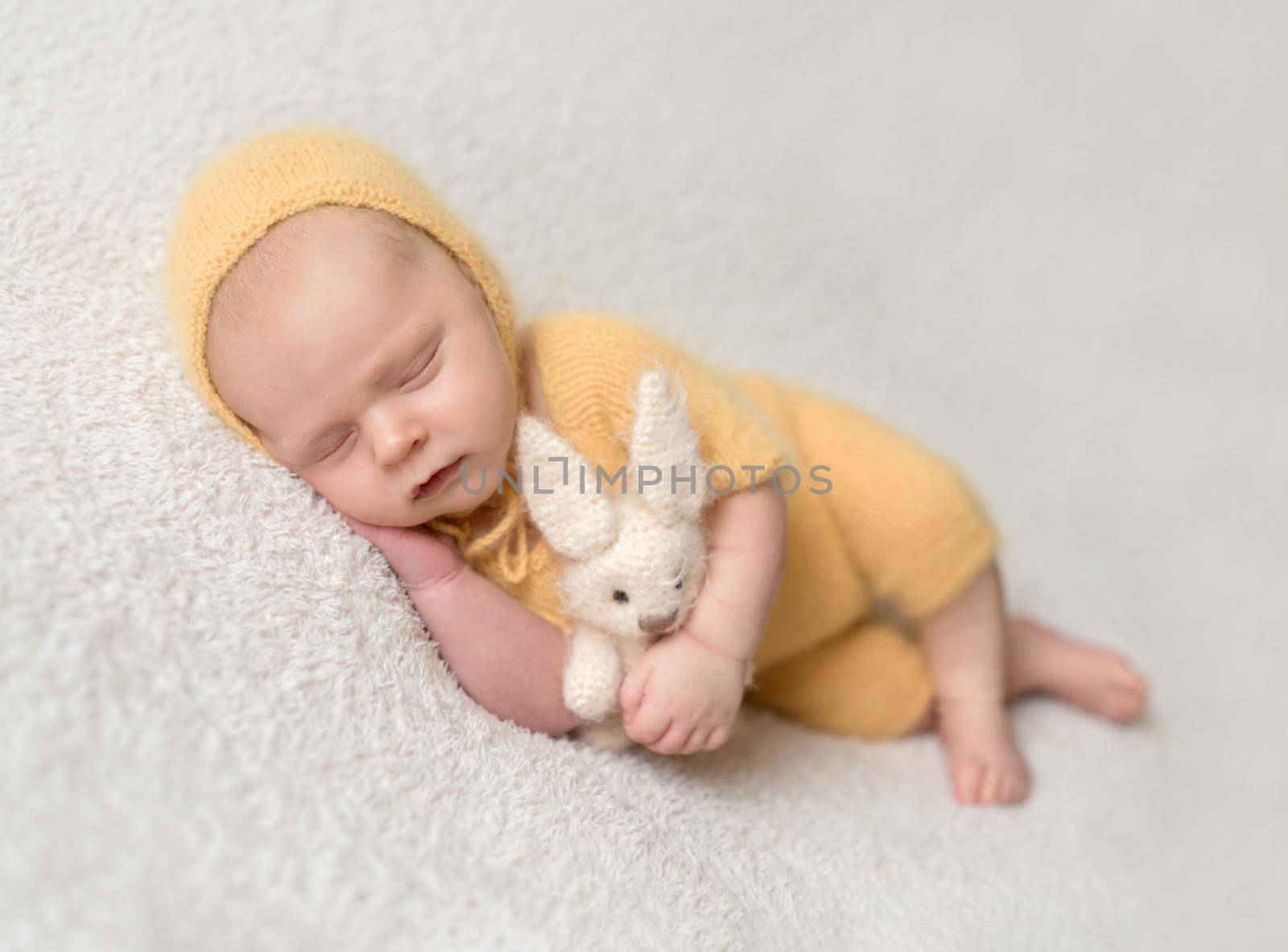 Little baby weared in cute yellow knitted suit sweetly sleeping on the white soft bedcover