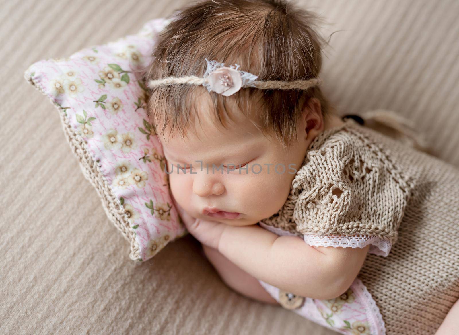 Cute little baby in knitted beanie and skirt sweetly sleeping on the light coverlet