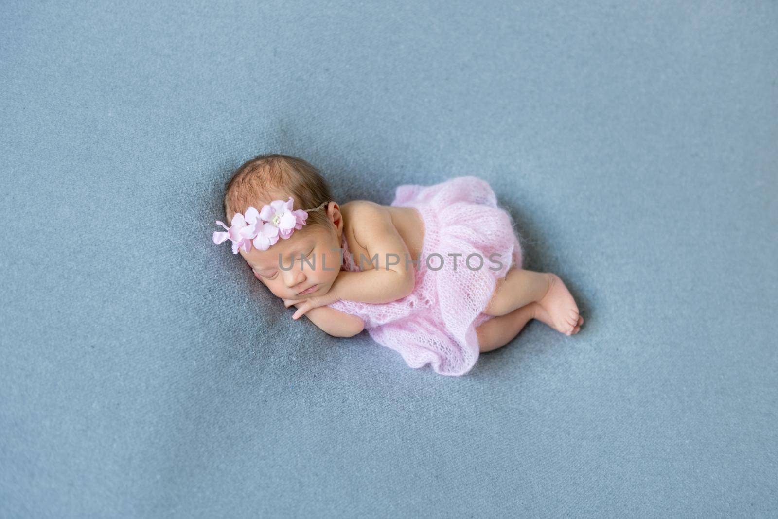 Sweet baby girl sleeping on her tummy, wearing pink little dress, in a flowery hairband