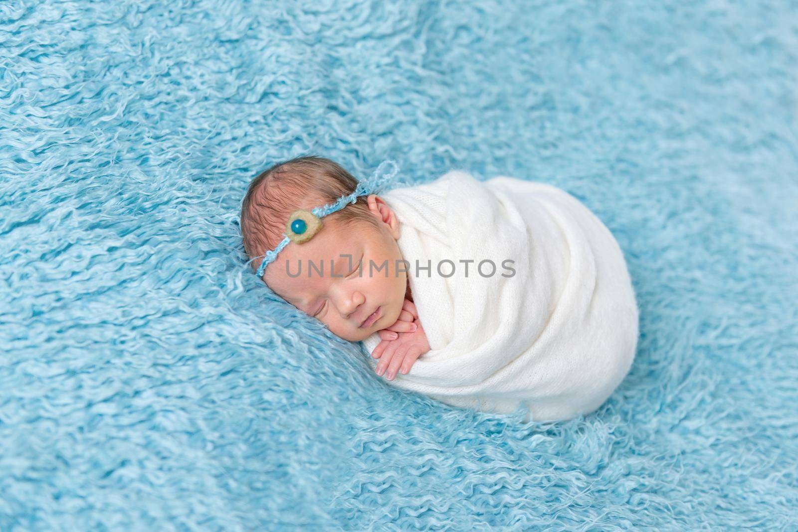 Adorable girl in flowery headband sleeping on her side, enveloped tightly in warm blanket